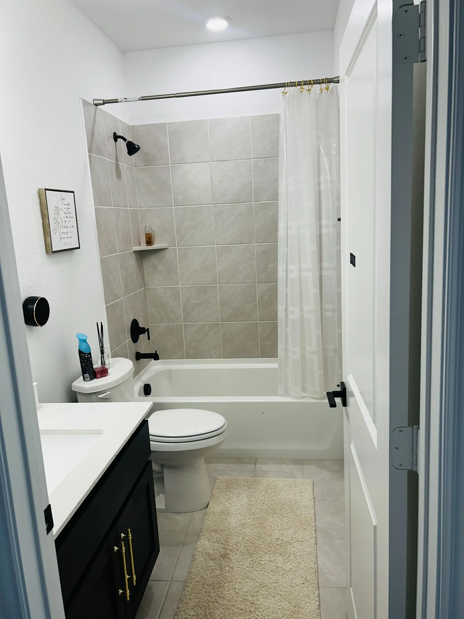 White subway tile shower surround with integrated shelf, black-finish fixtures, white vanity with black cabinetry, and gold-tone hardware