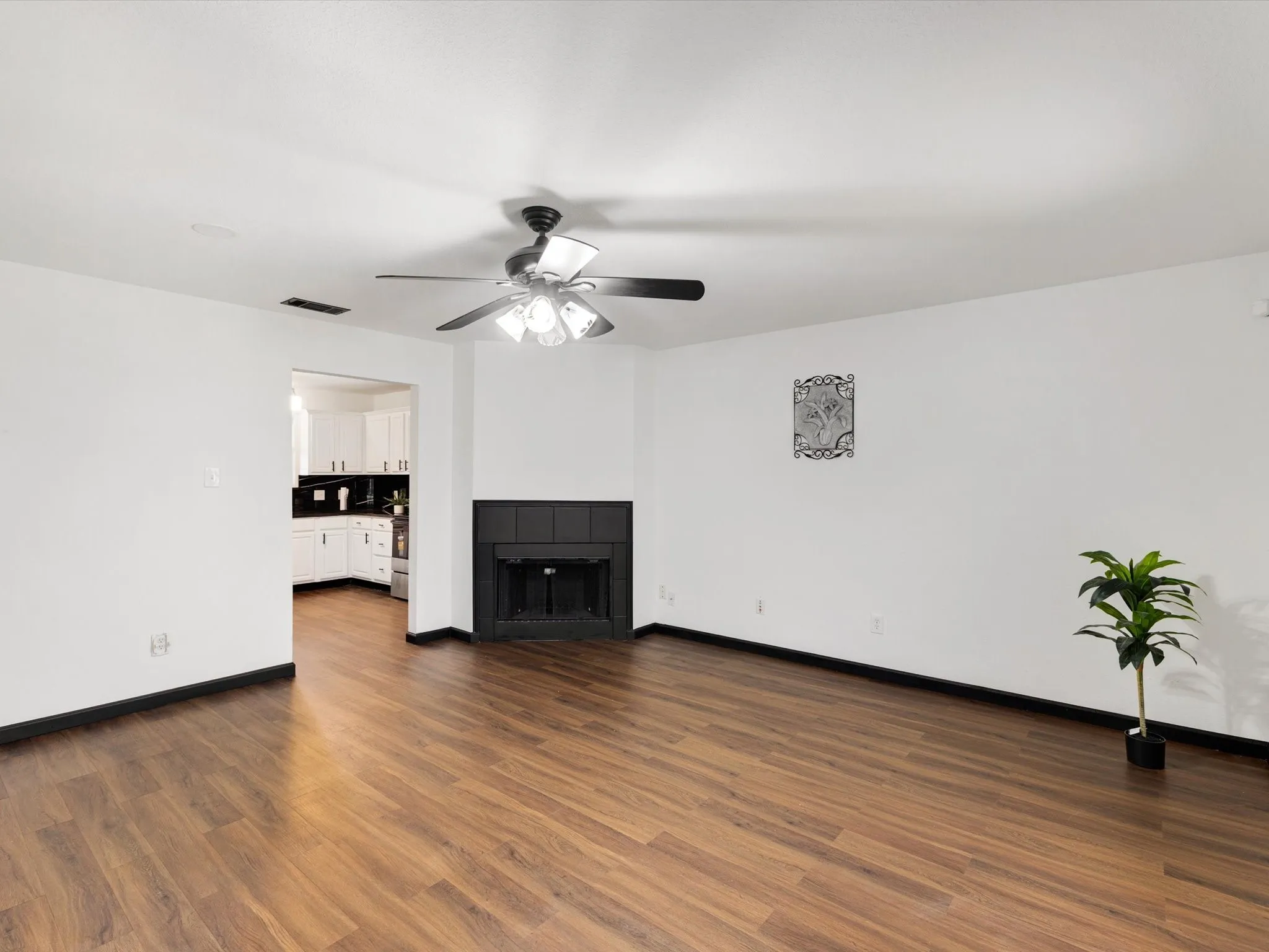 Wood-finish flooring, corner fireplace with a black surround, white walls, and a ceiling fan with light fixture
