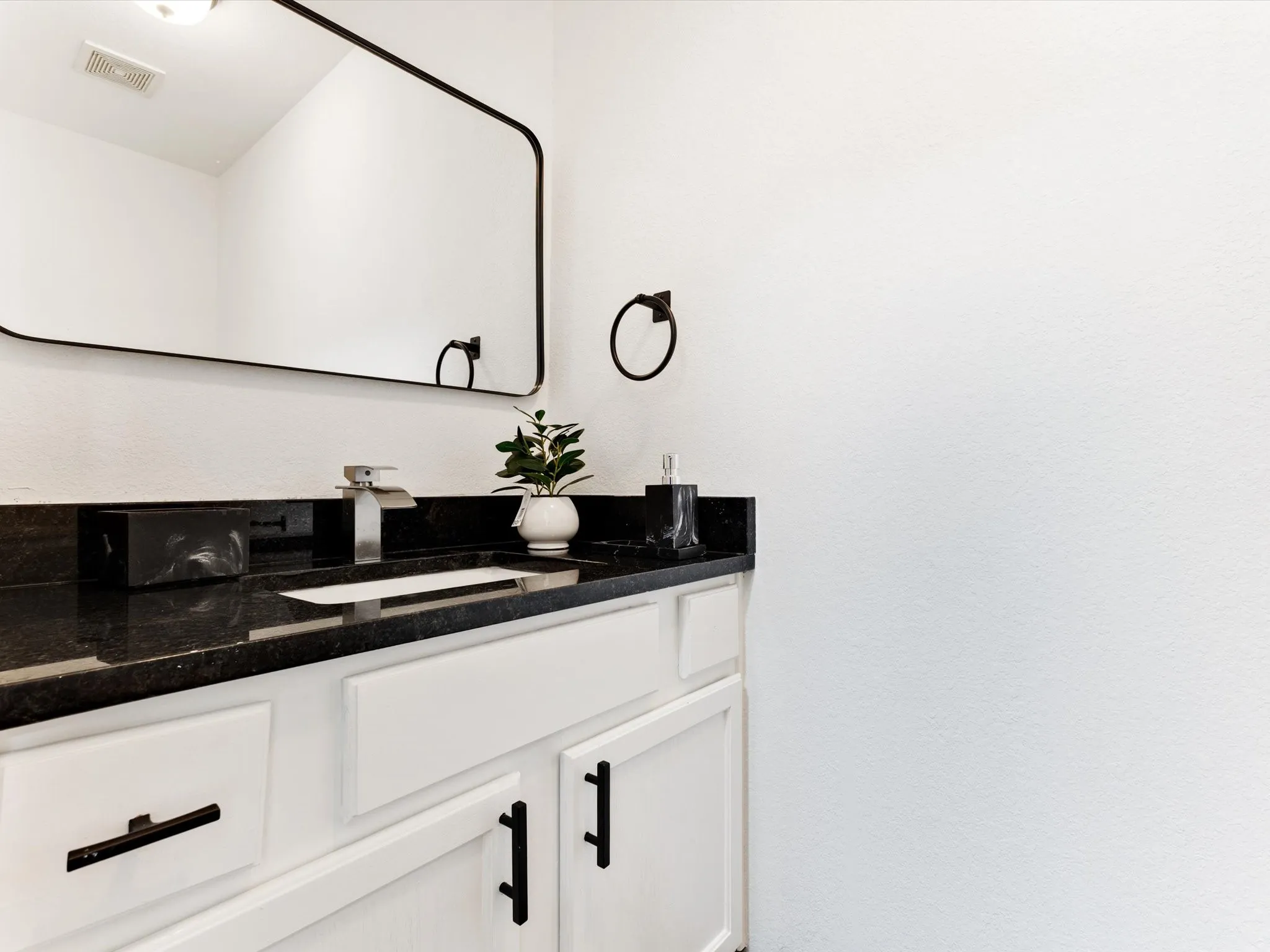 White vanity with black hardware, black countertop, rectangular vessel sink, and wall-mounted mirror
