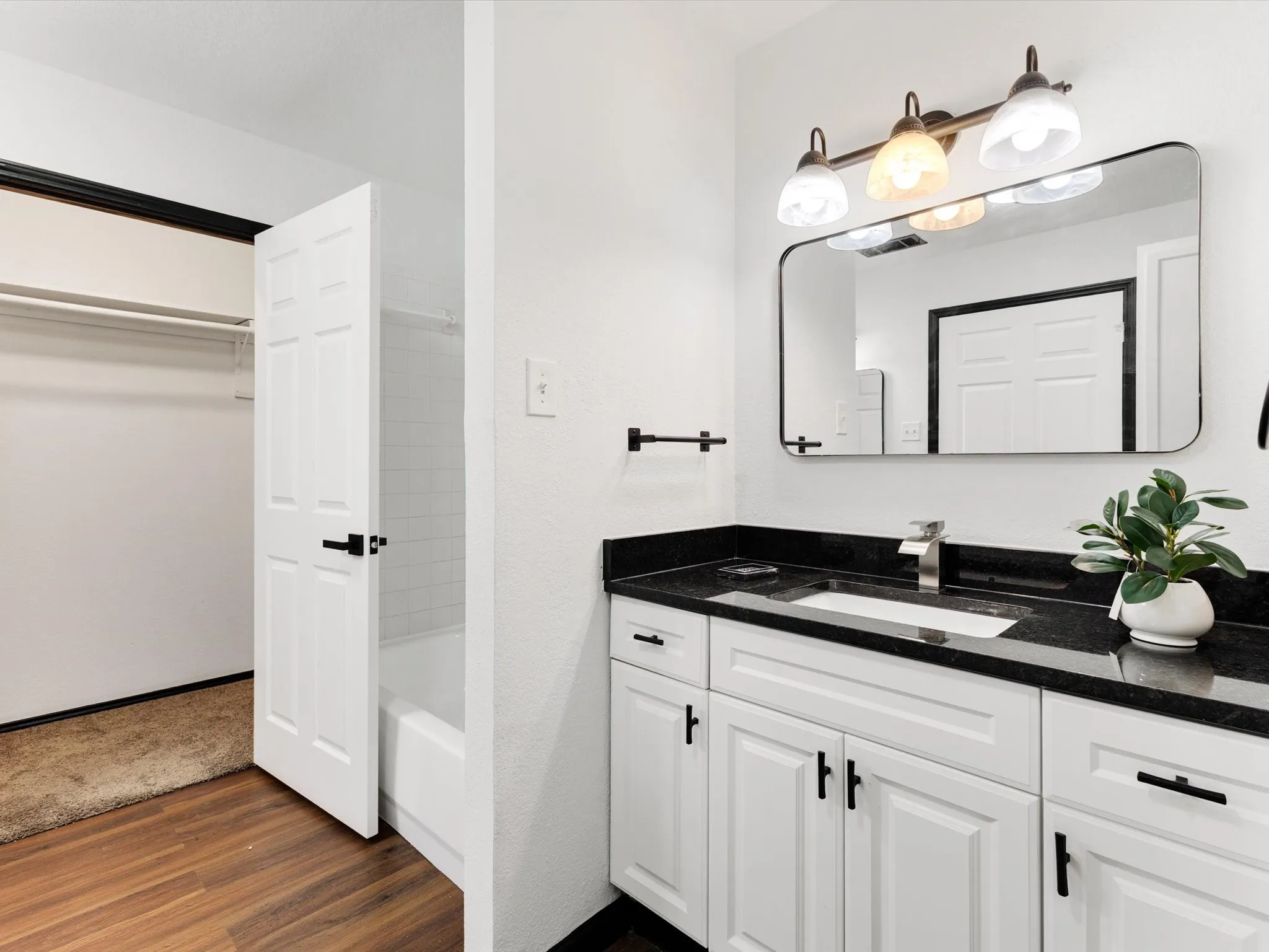 White vanity with black hardware, black countertop, rectangular undermount sink, and a framed mirror