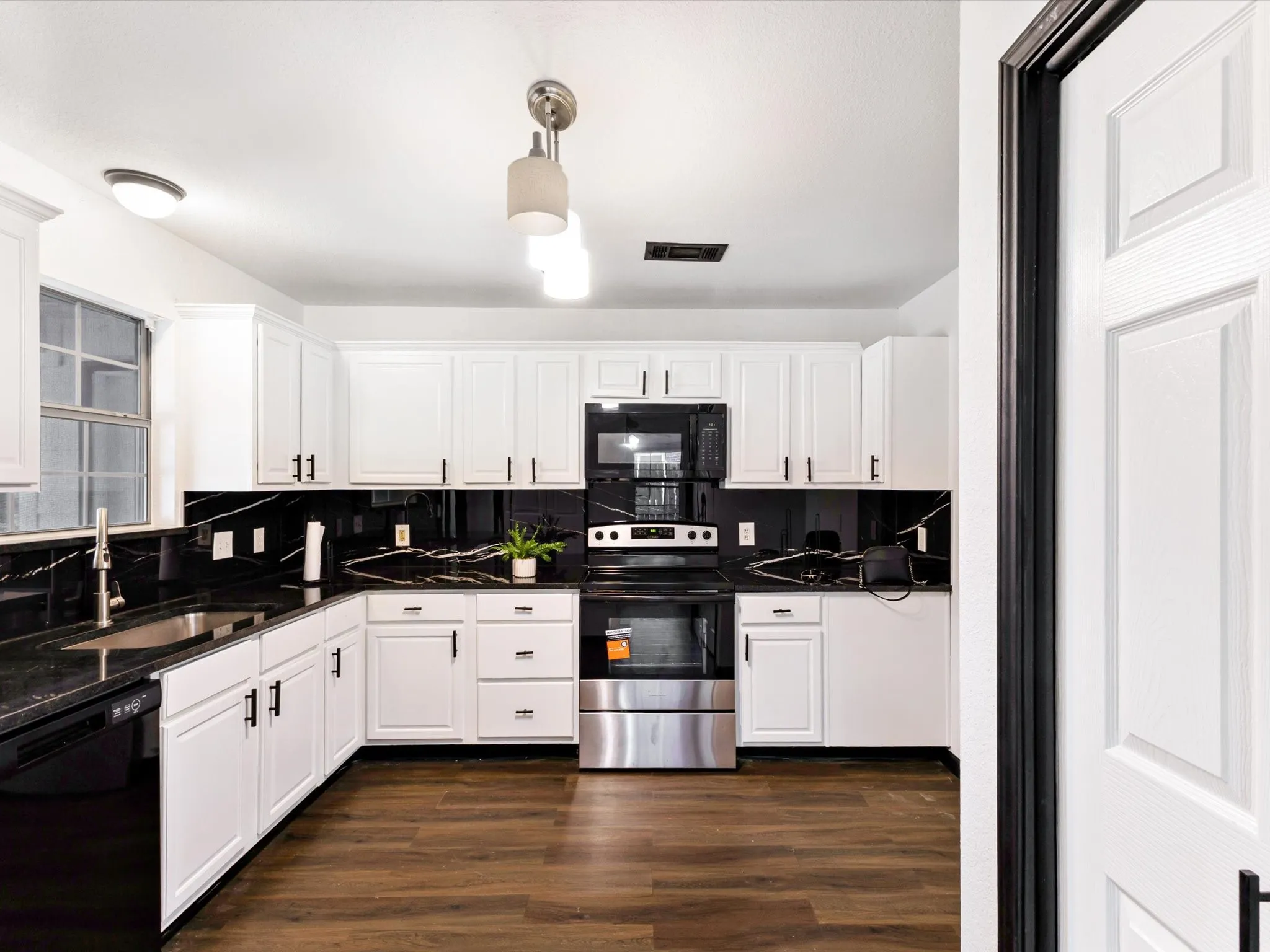 White shaker cabinetry with matte black hardware, black countertops with integrated sink, black backsplash, stainless steel appliances, and wood-finish flooring