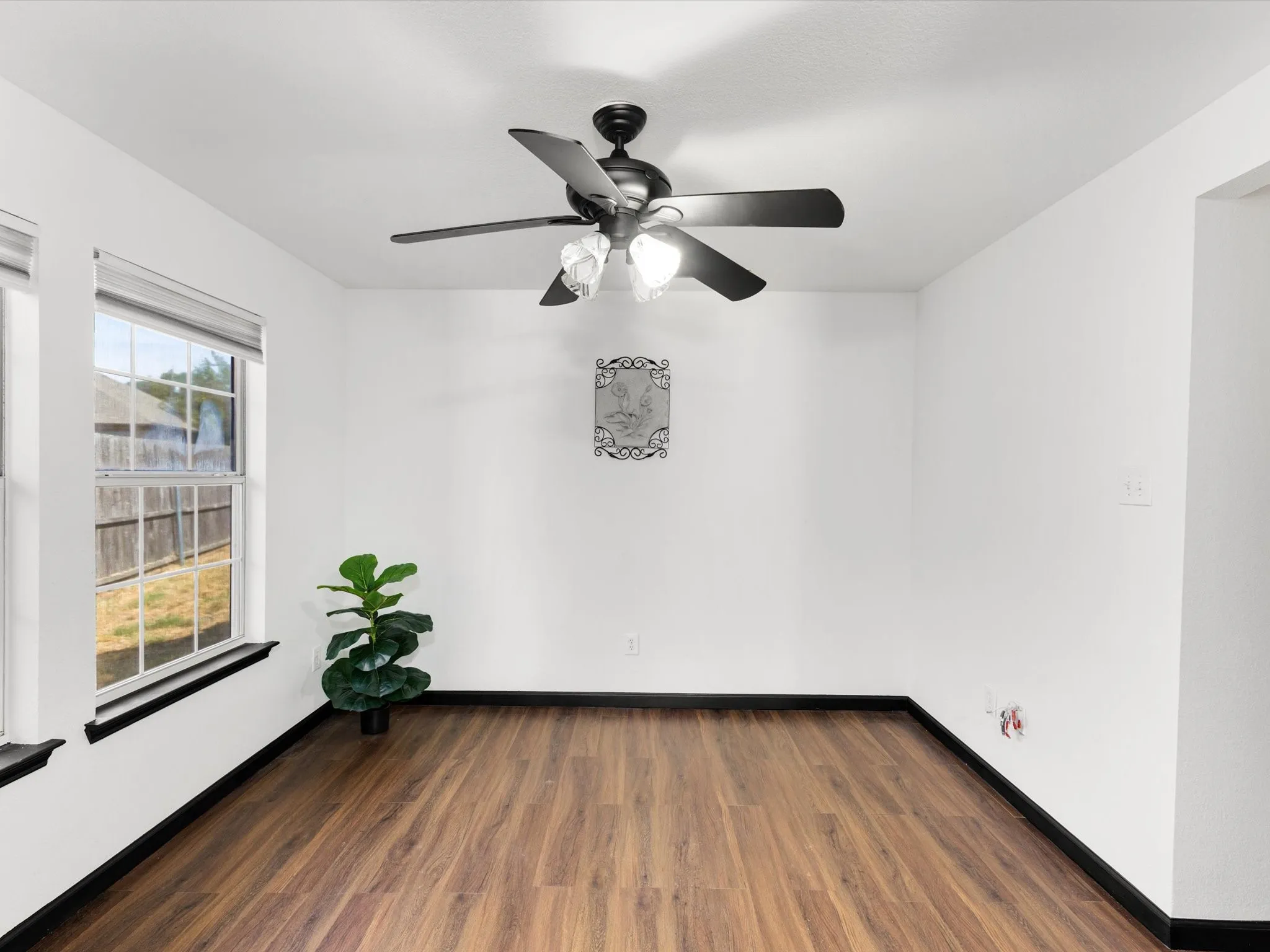 Wood-finish flooring, white painted walls, and a ceiling fan with integrated lighting