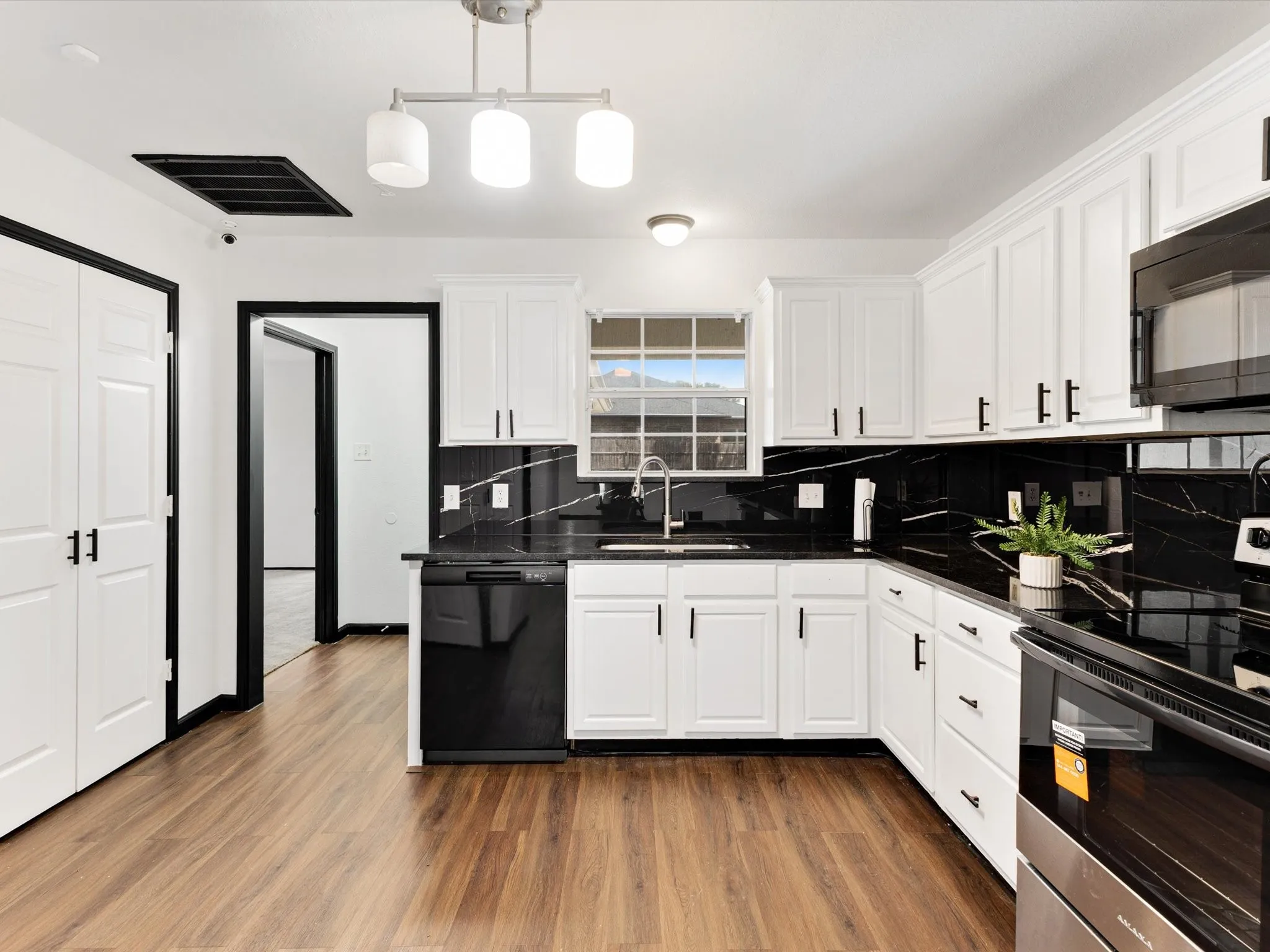 Kitchen featuring wood-finish flooring, white cabinetry with dark hardware, black countertops, and a black tile backsplash