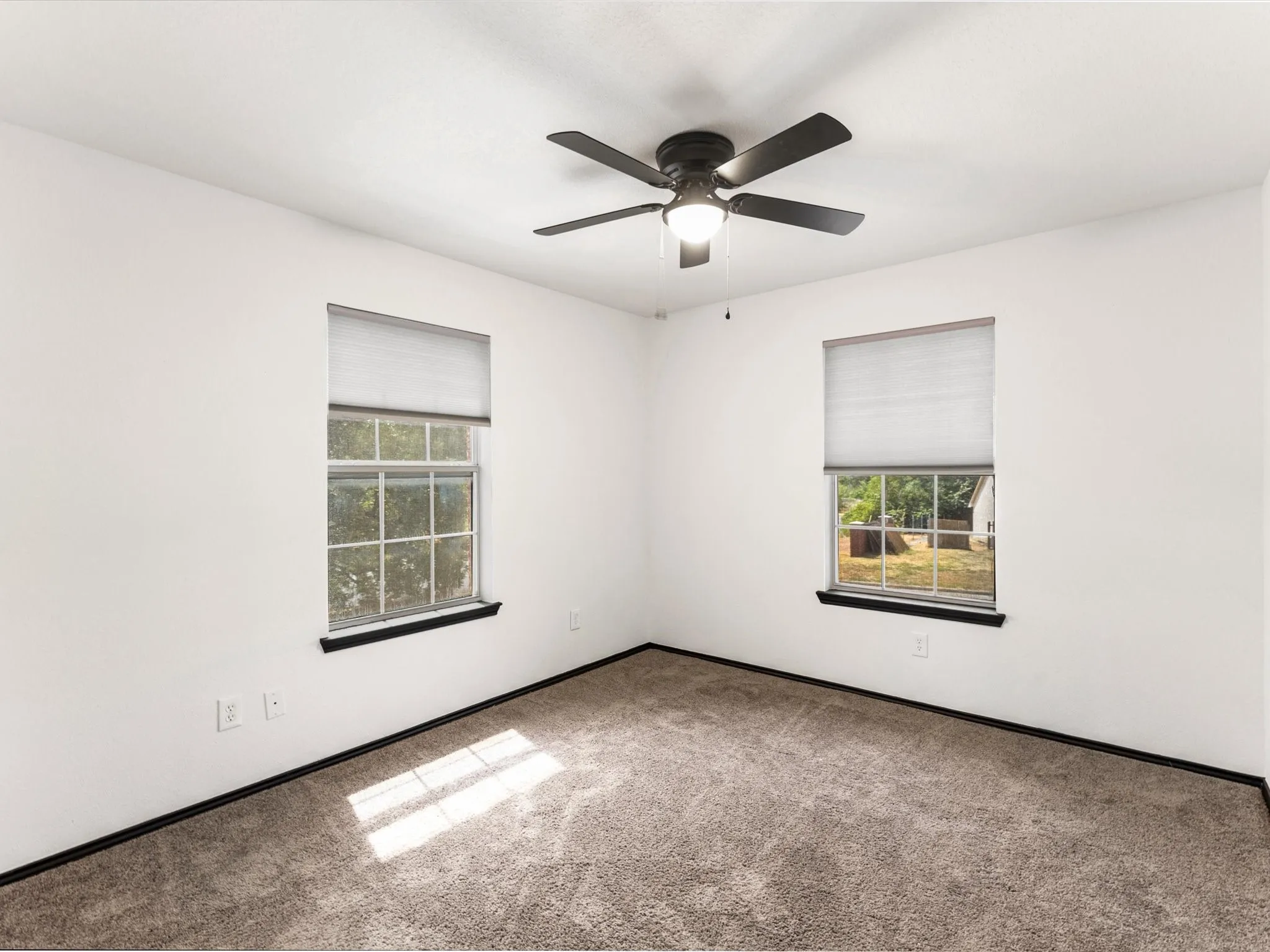 Neutral wall color, carpet flooring, windows with roller shades, and a ceiling fan with integrated lighting