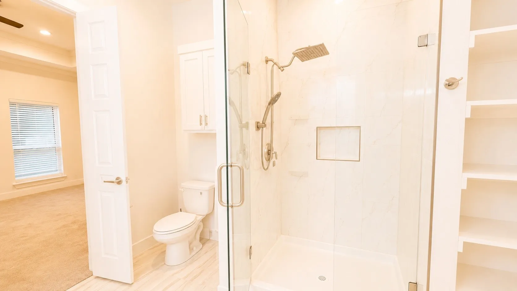 Glass-enclosed shower with a rainfall showerhead, handheld shower fixture, and recessed shower niche