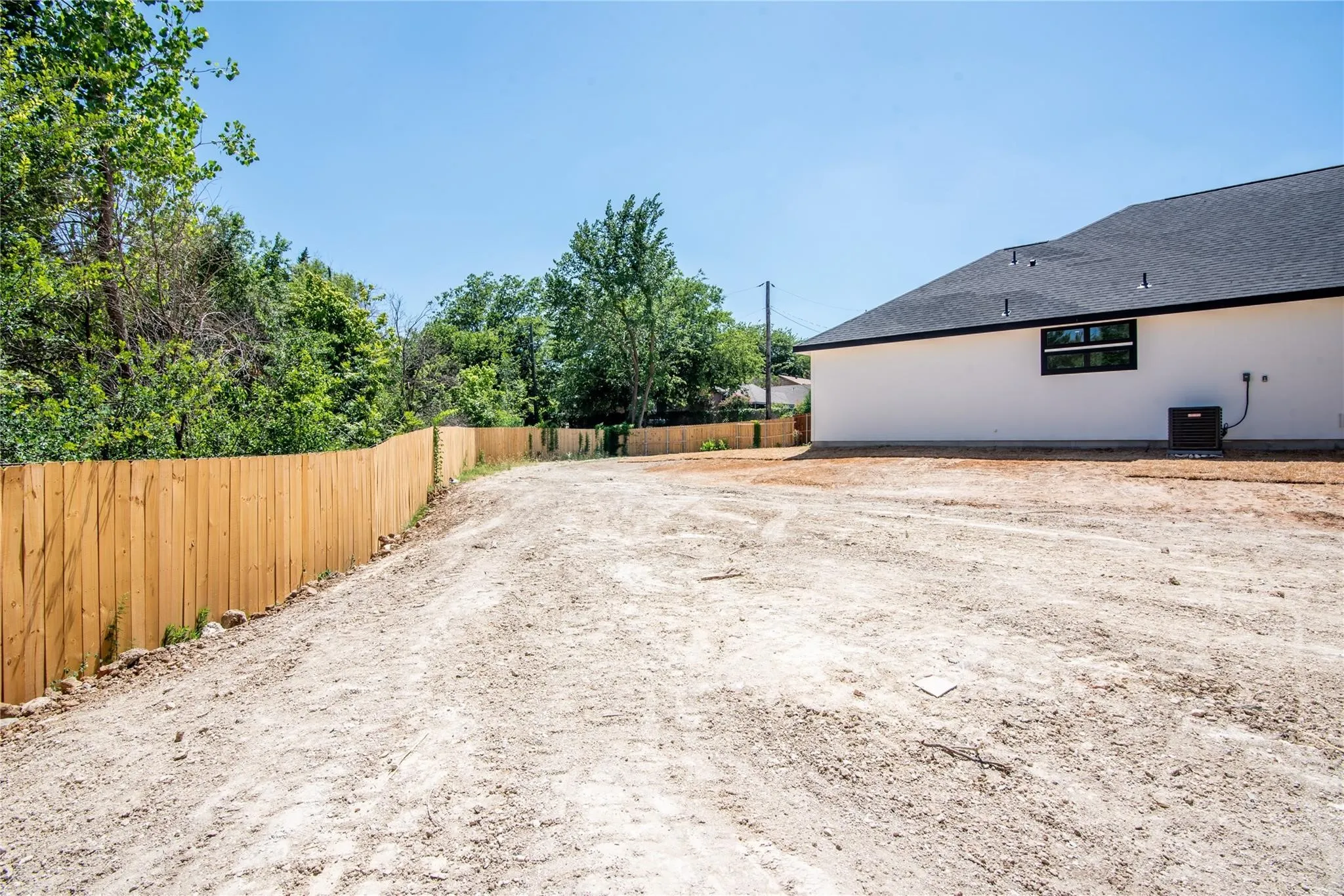 Spacious rear property area with a newly constructed wood fence, white exterior siding, a dark roof, and a visible HVAC unit