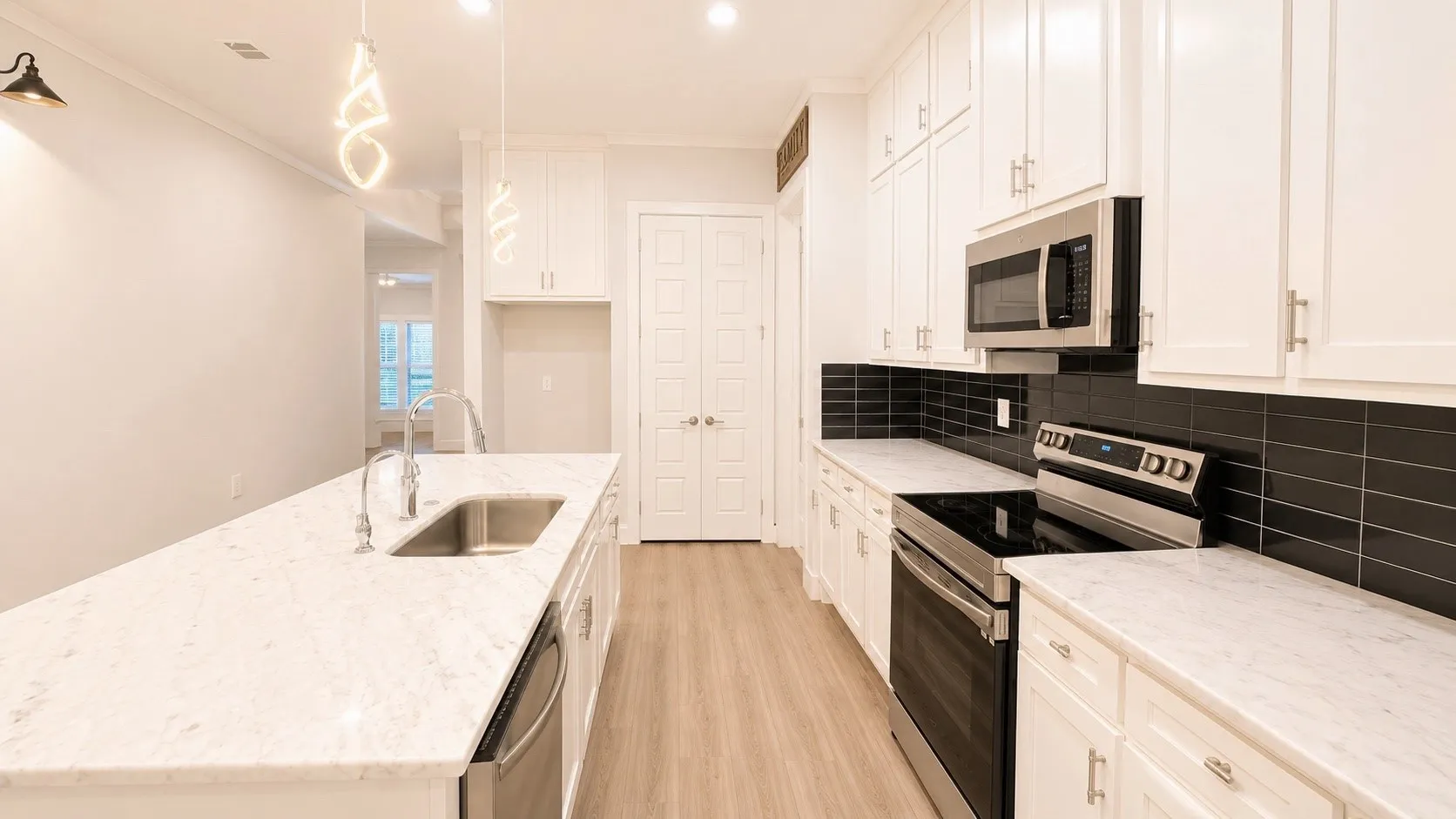 Kitchen featuring white cabinetry, stainless steel appliances, a large island with an undermount sink, black subway tile backsplash, and light wood-finish flooring