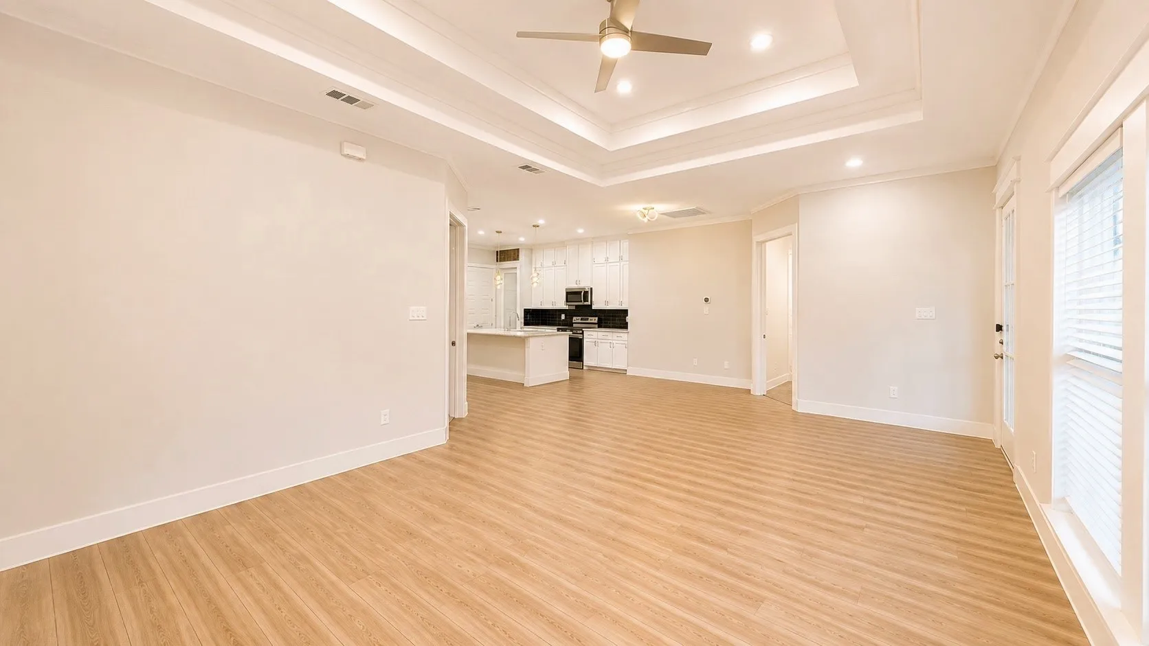 Wood-finish flooring throughout the main living area, featuring a tray ceiling with recessed lighting and a ceiling fan