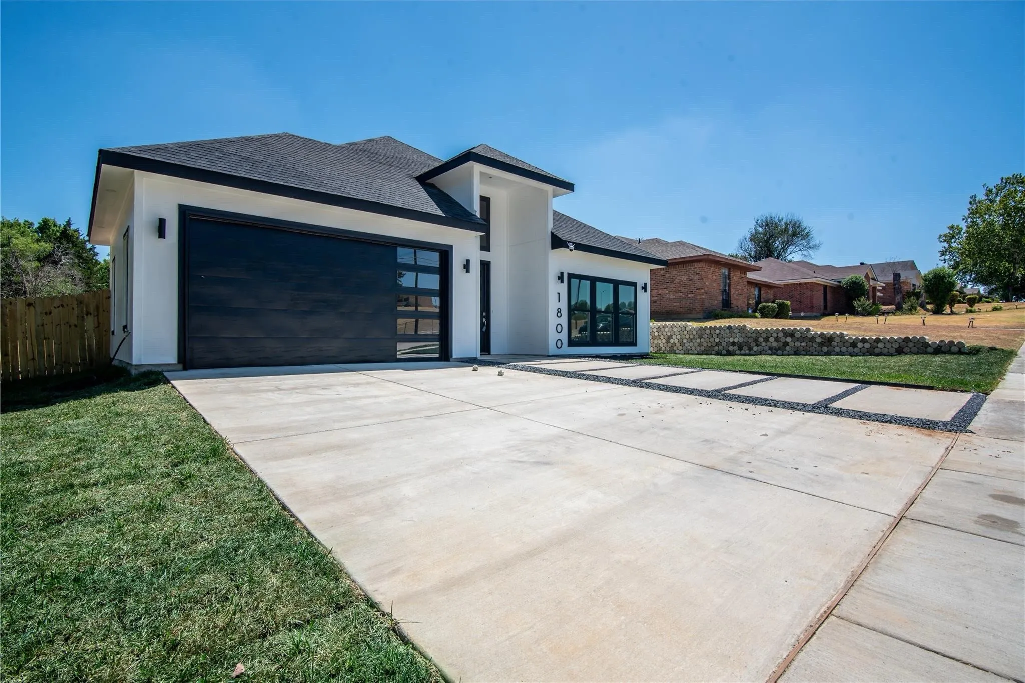 Contemporary exterior with white stucco finish, dark framed windows, a black garage door with frosted glass panels, and a concrete driveway