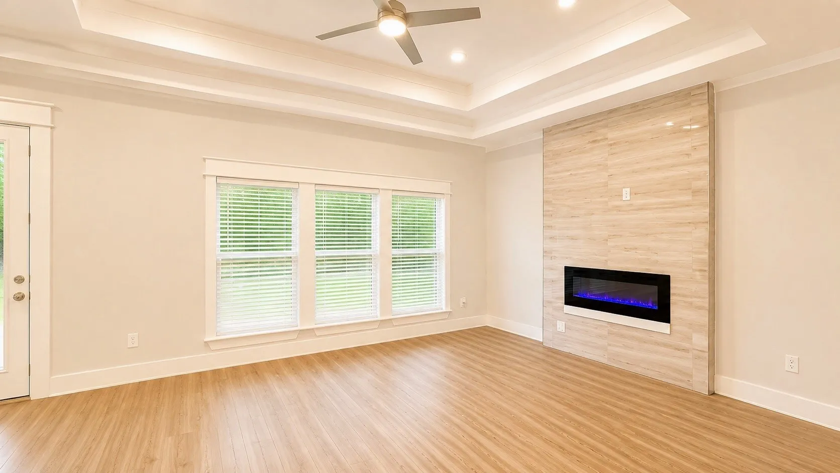 Wood-finish flooring, tray ceiling with recessed lighting, ceiling fan, and an electric fireplace with a tiled surround