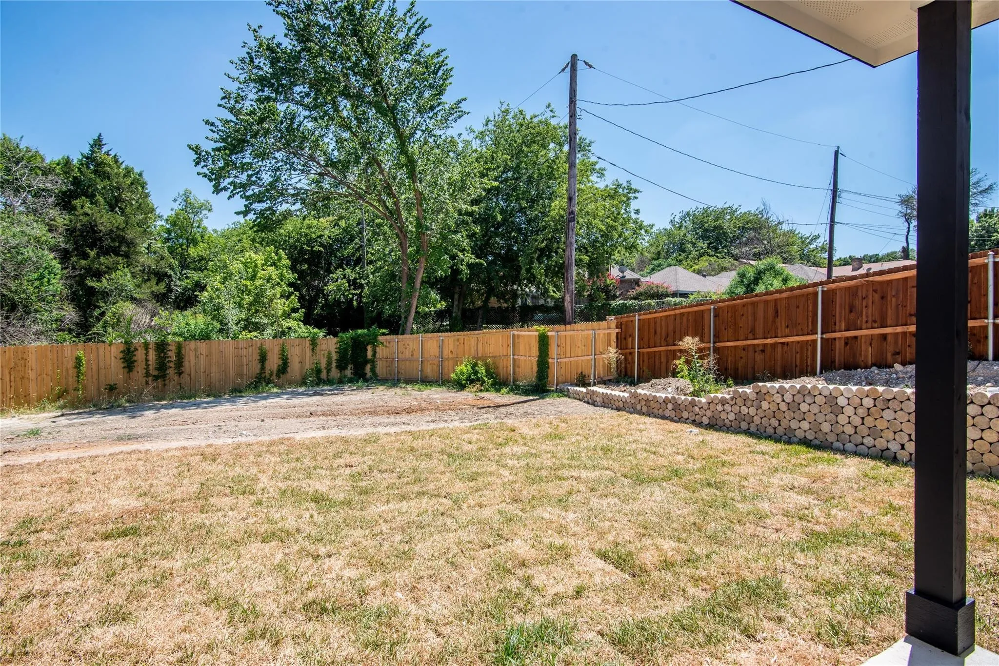 Expansive backyard featuring a wood privacy fence, decorative wood retaining wall, and a covered patio area
