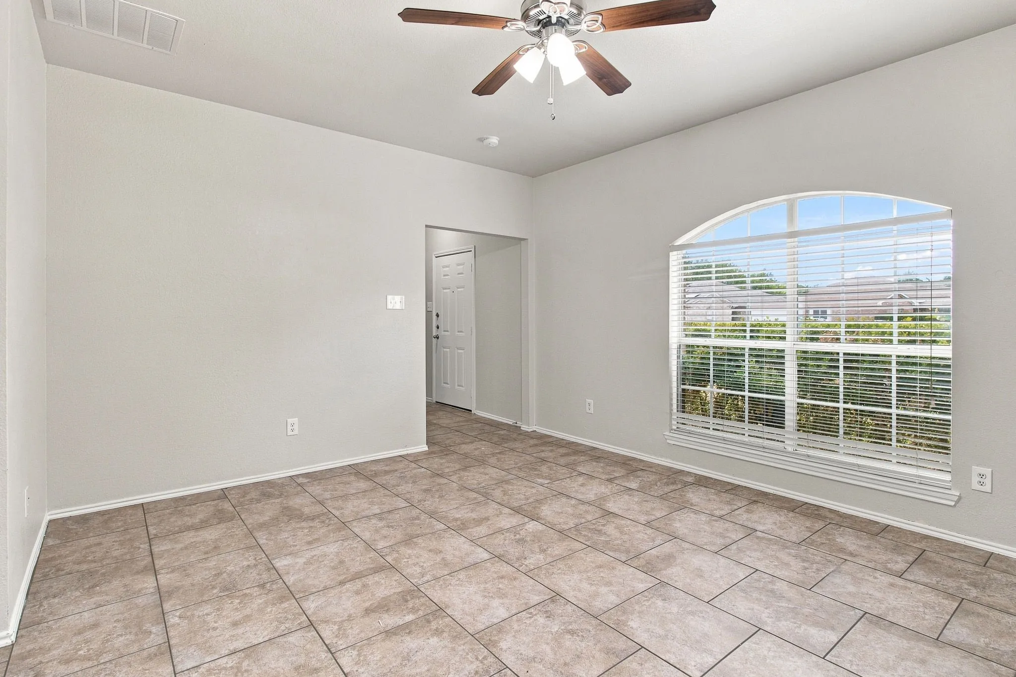 Spacious room featuring tile flooring, neutral wall tones, an arched window with blinds, and a ceiling fan with light fixture