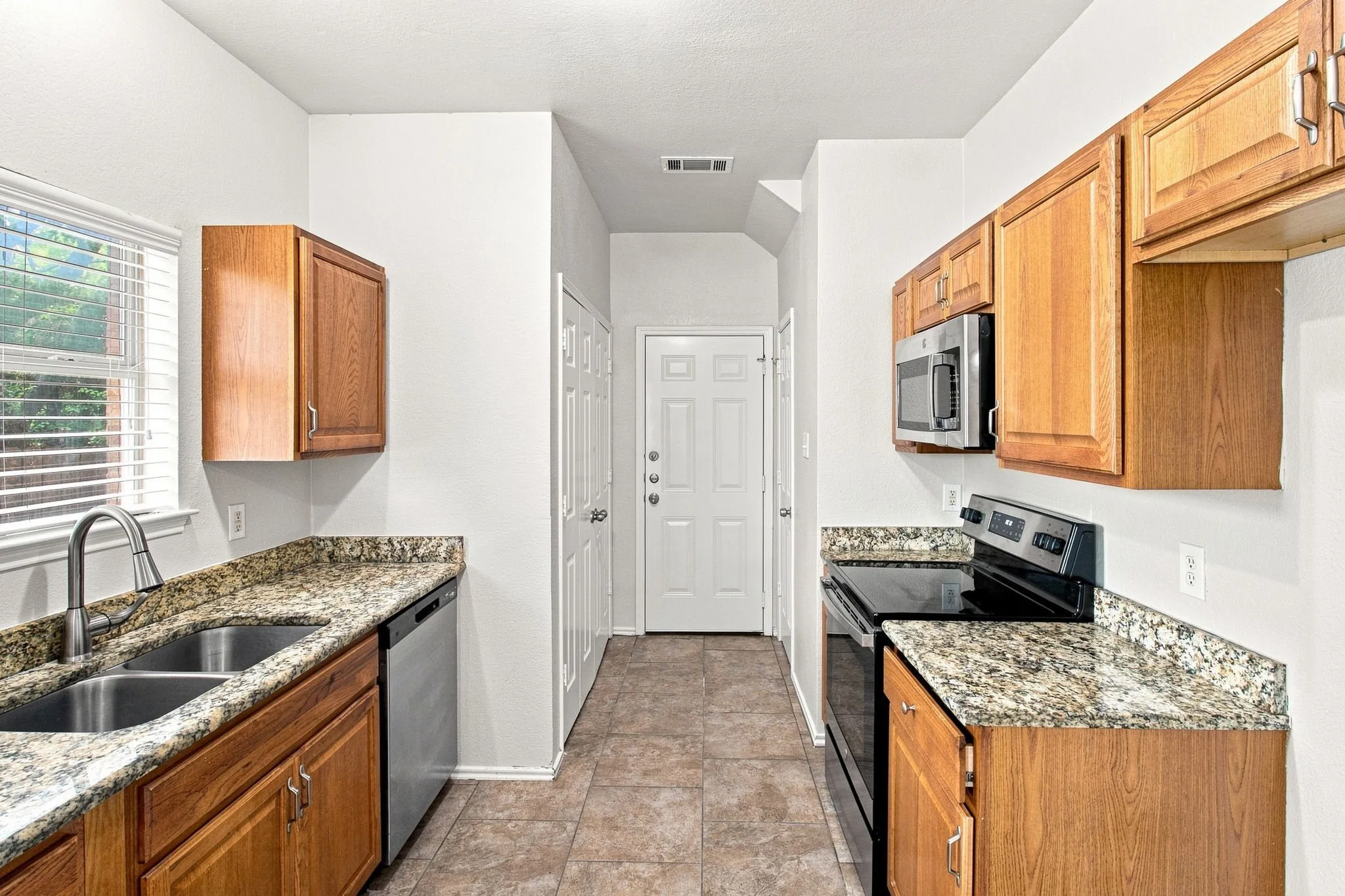 Kitchen featuring wood cabinetry, granite countertops, stainless steel appliances, and tile flooring