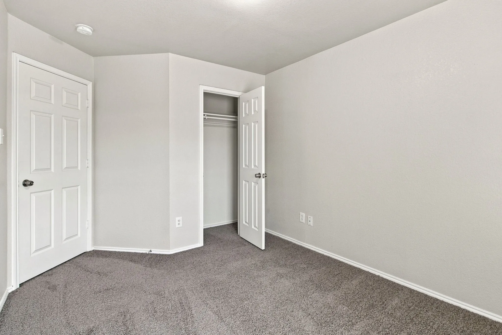Neutral wall paint with textured carpeting, a flush-mount ceiling light, and a built-in closet with shelving and hanging rods