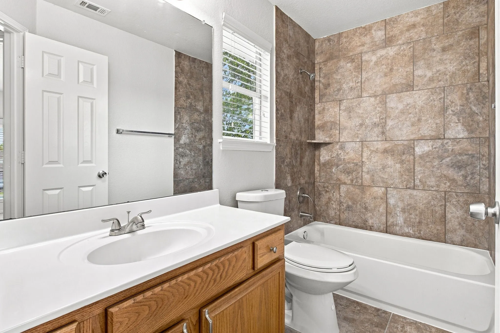 Bathroom featuring a wood-finish vanity with an integrated sink, a full-width mirror, and a tiled shower/tub combination with a built-in shelf