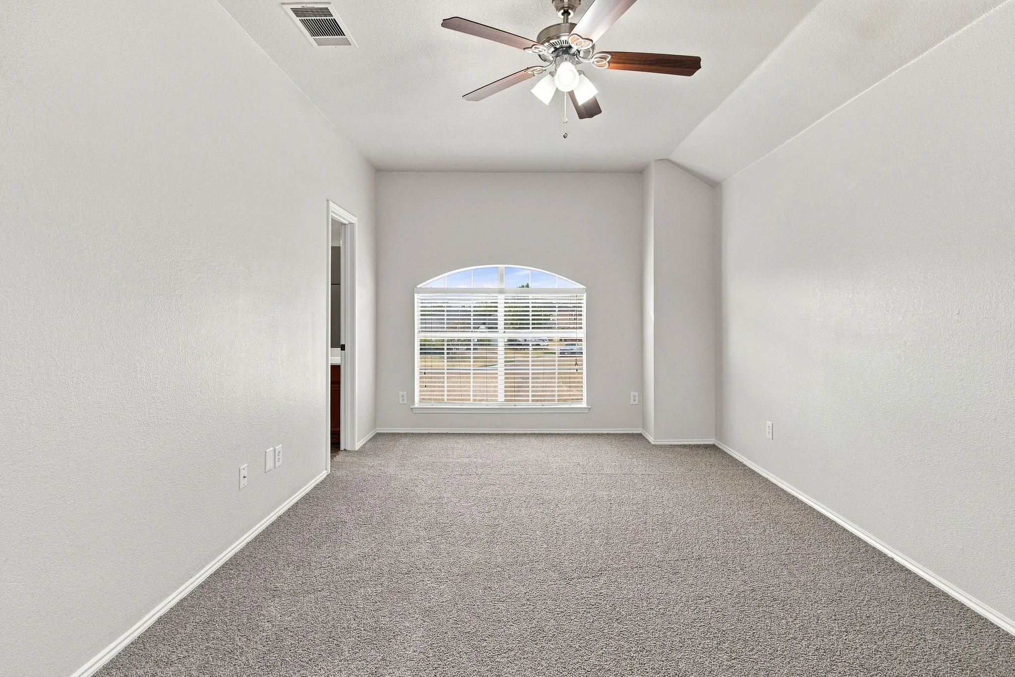 Arched window with blinds, ceiling fan, and grey carpeting