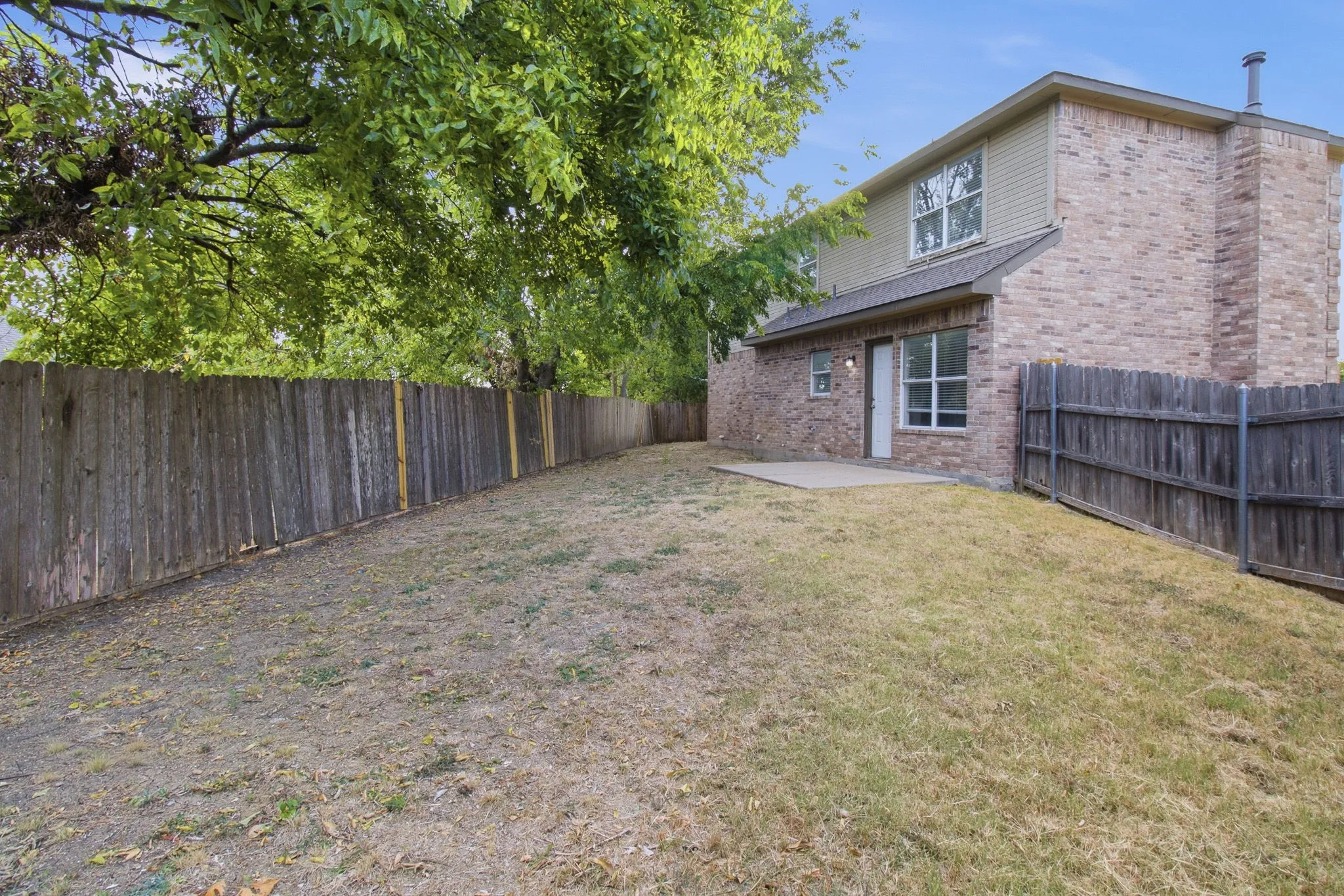Expansive backyard featuring a privacy fence, concrete patio, and mature trees