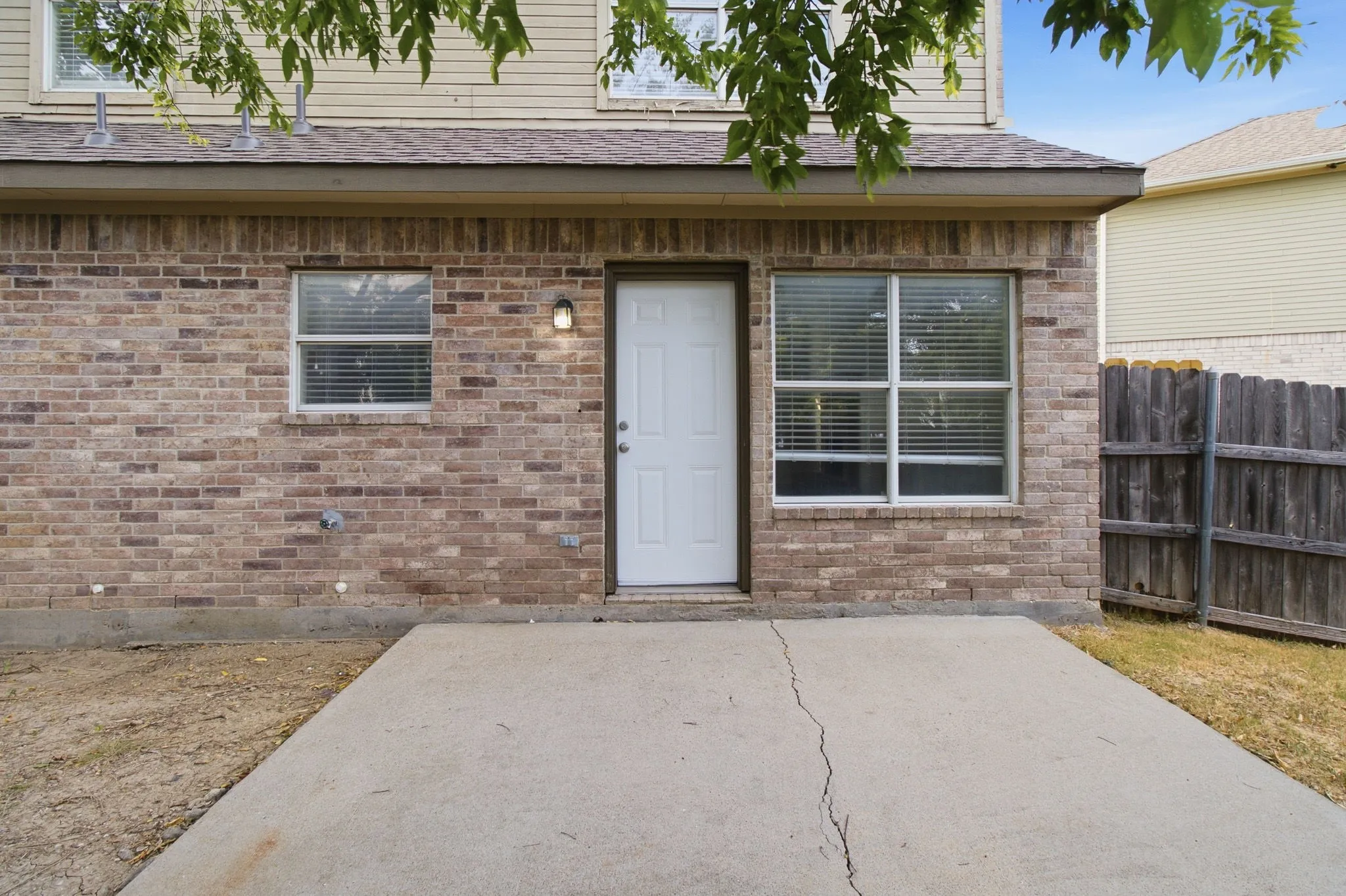 Brick exterior with a concrete patio, exterior lighting fixture, and white rear entry door