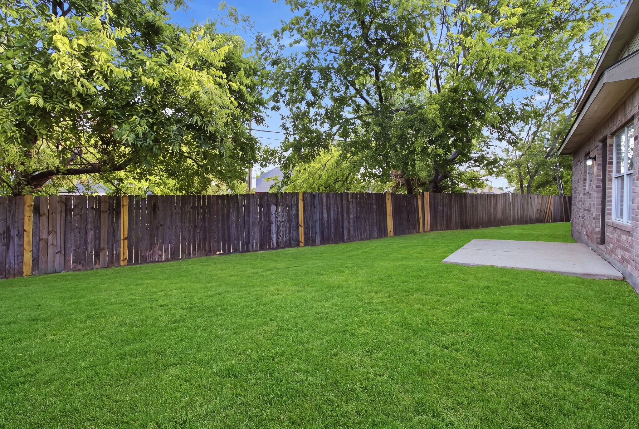 Expansive lawn featuring mature trees and wood fencing
