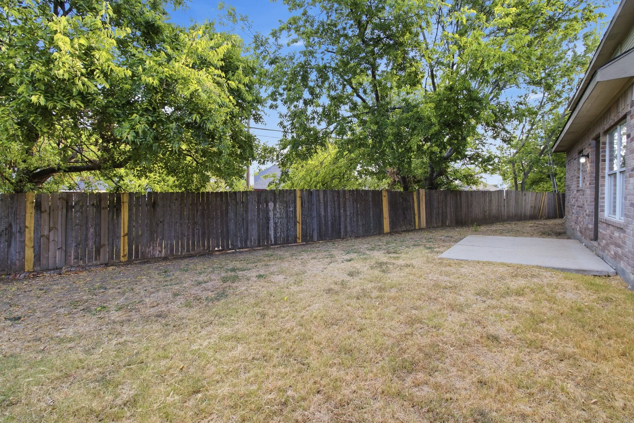 Expansive backyard featuring a wood privacy fence, concrete patio, and mature trees