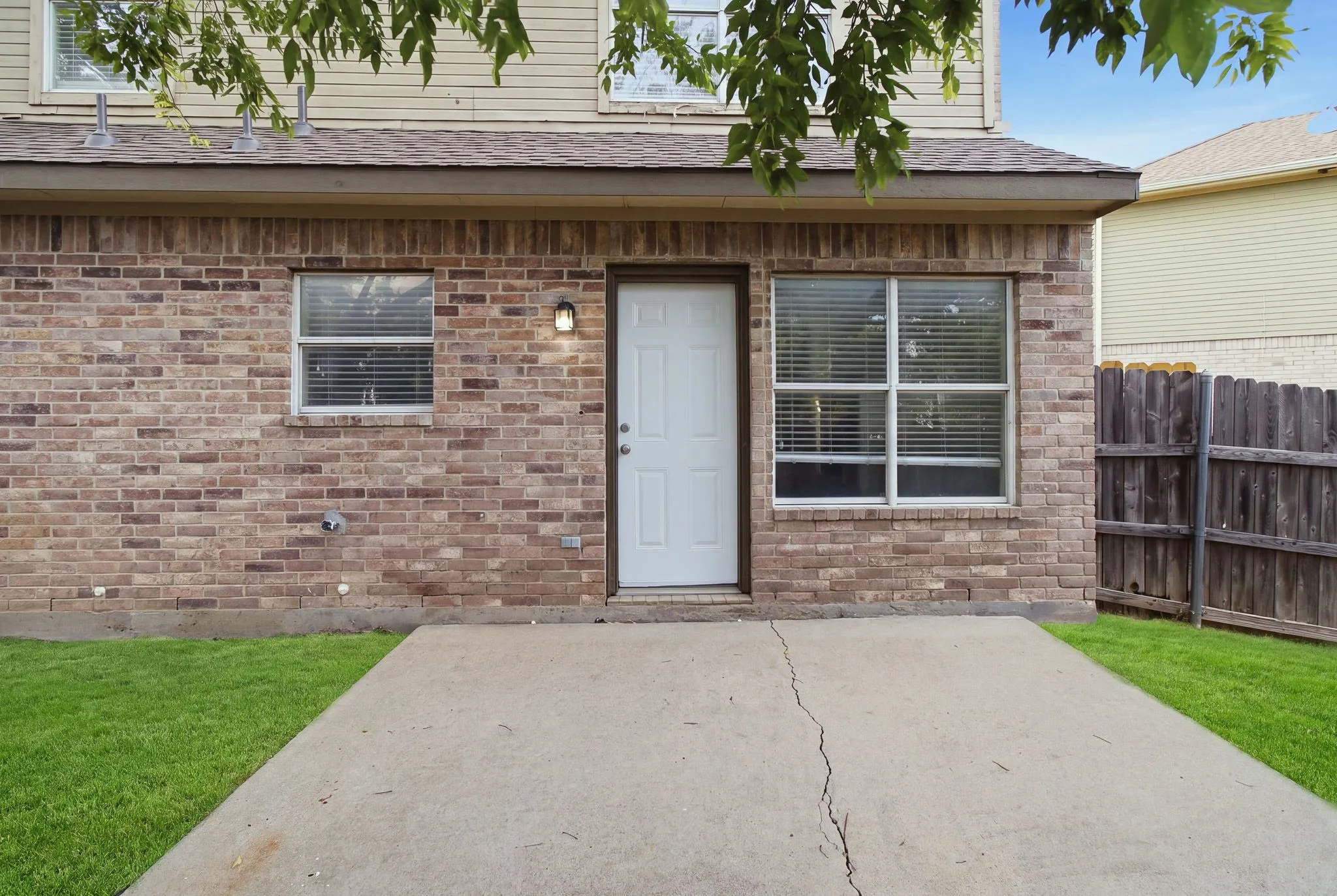 Brick exterior with a white door, concrete patio, and a privacy fence