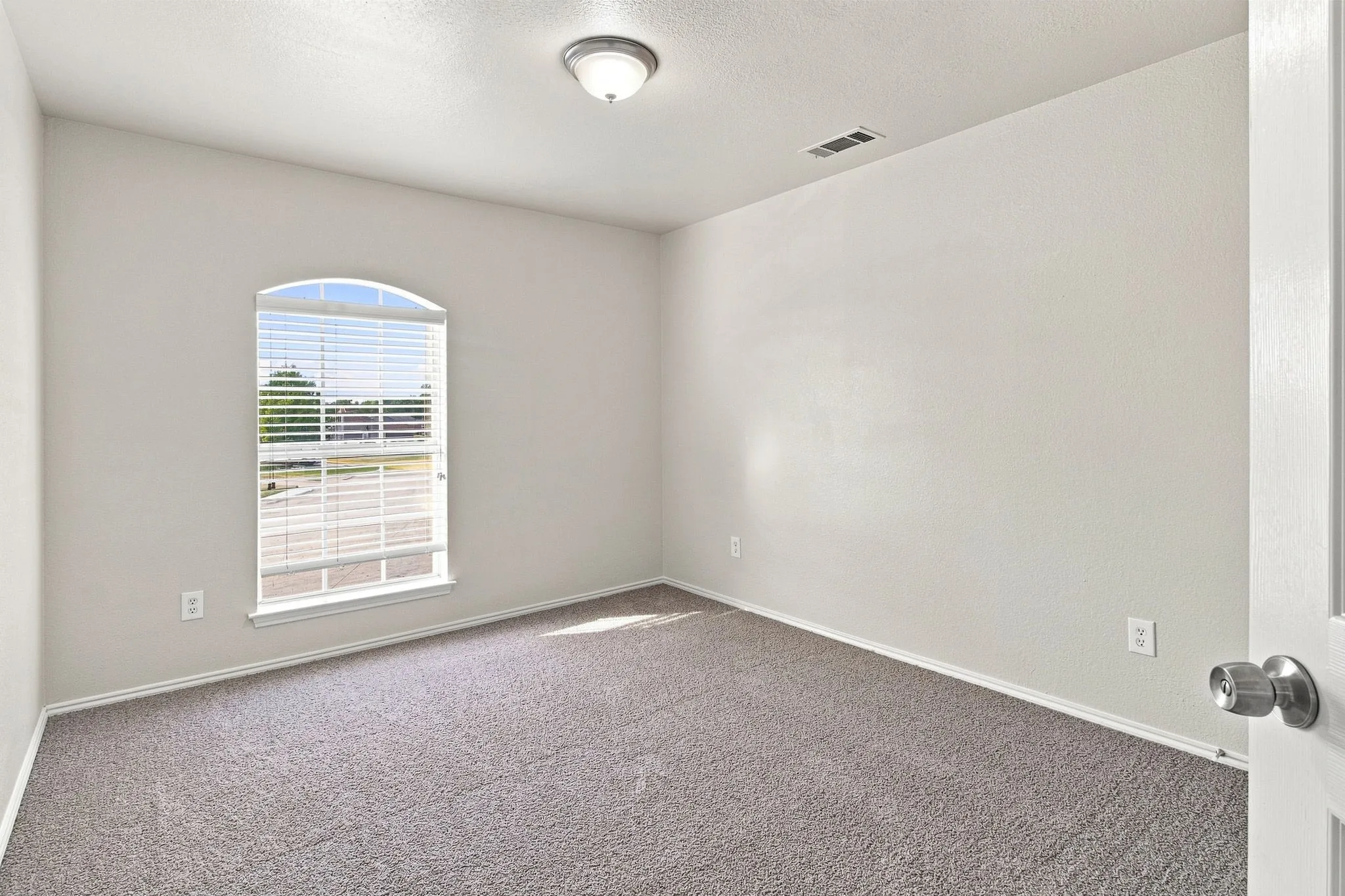 Arched window with blinds, carpeted flooring, and a flush-mount ceiling light fixture