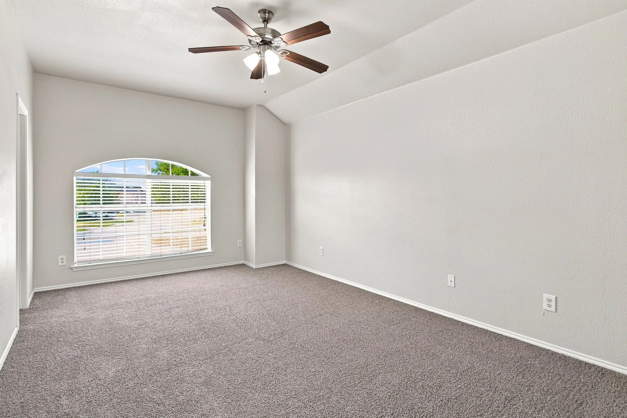 Vaulted ceiling with a ceiling fan, arched window, and neutral carpeting