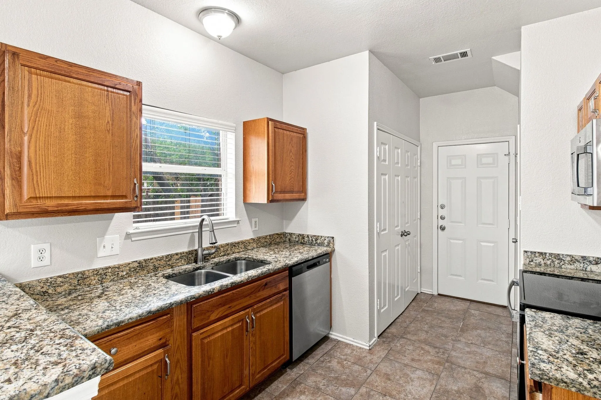 Kitchen featuring wood cabinetry, granite-finish countertops, stainless steel sink, stainless steel dishwasher, and tile flooring
