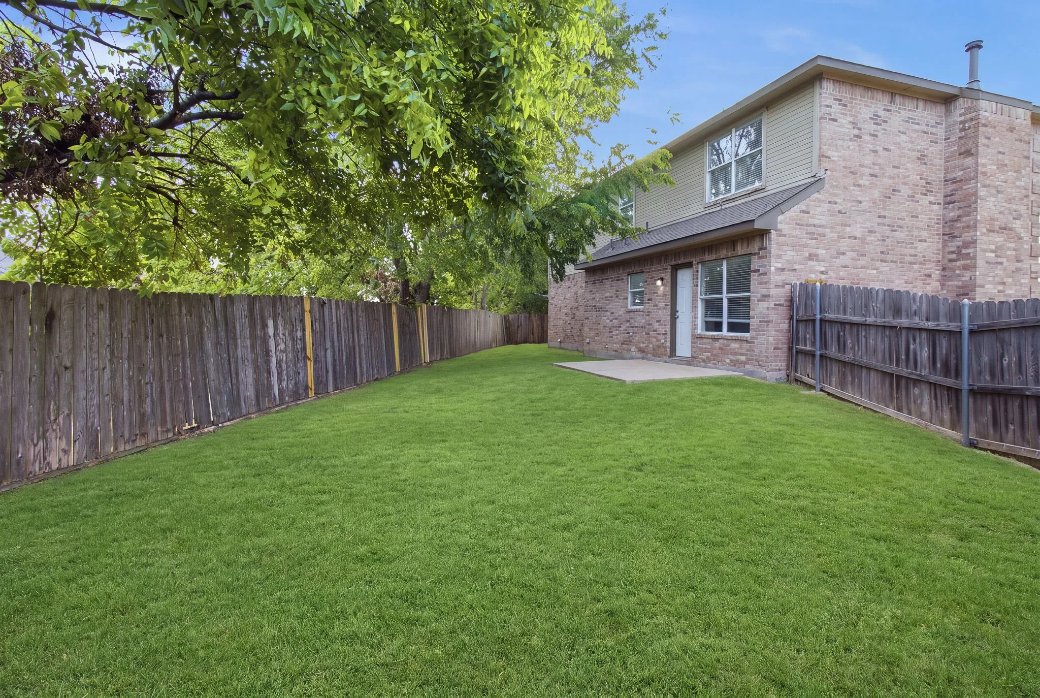 Expansive green lawn, wood privacy fence, concrete patio, brick exterior, and a second-story dormer window