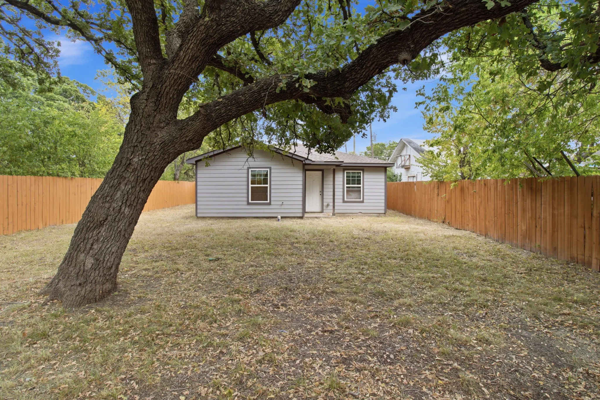 Expansive backyard featuring a mature tree, wood fencing, and a compact exterior