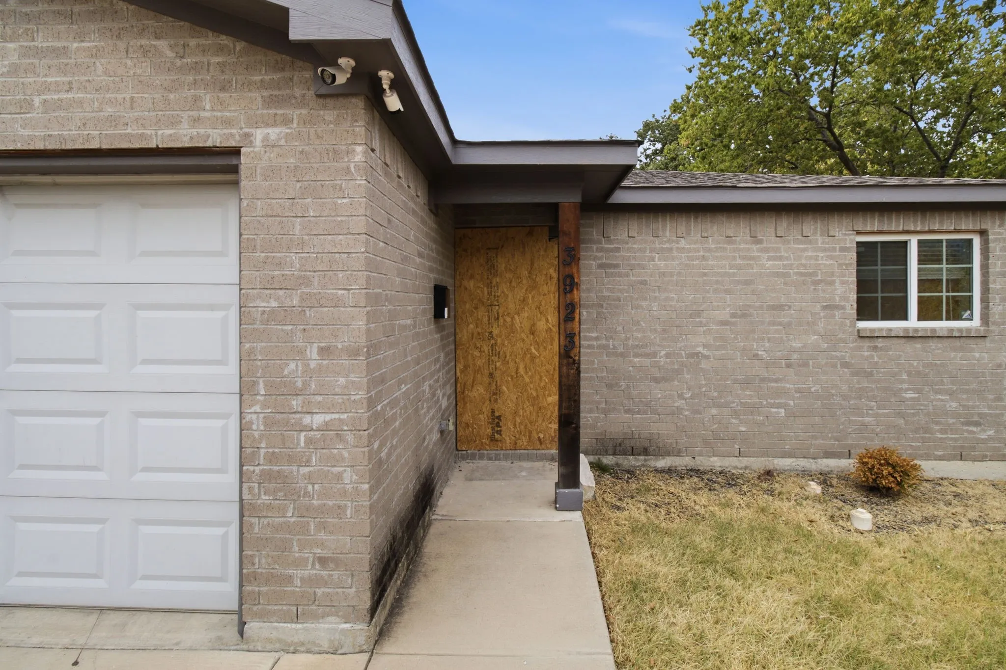 Brick exterior with an attached garage featuring a panel door, covered entryway, and a window with white framing