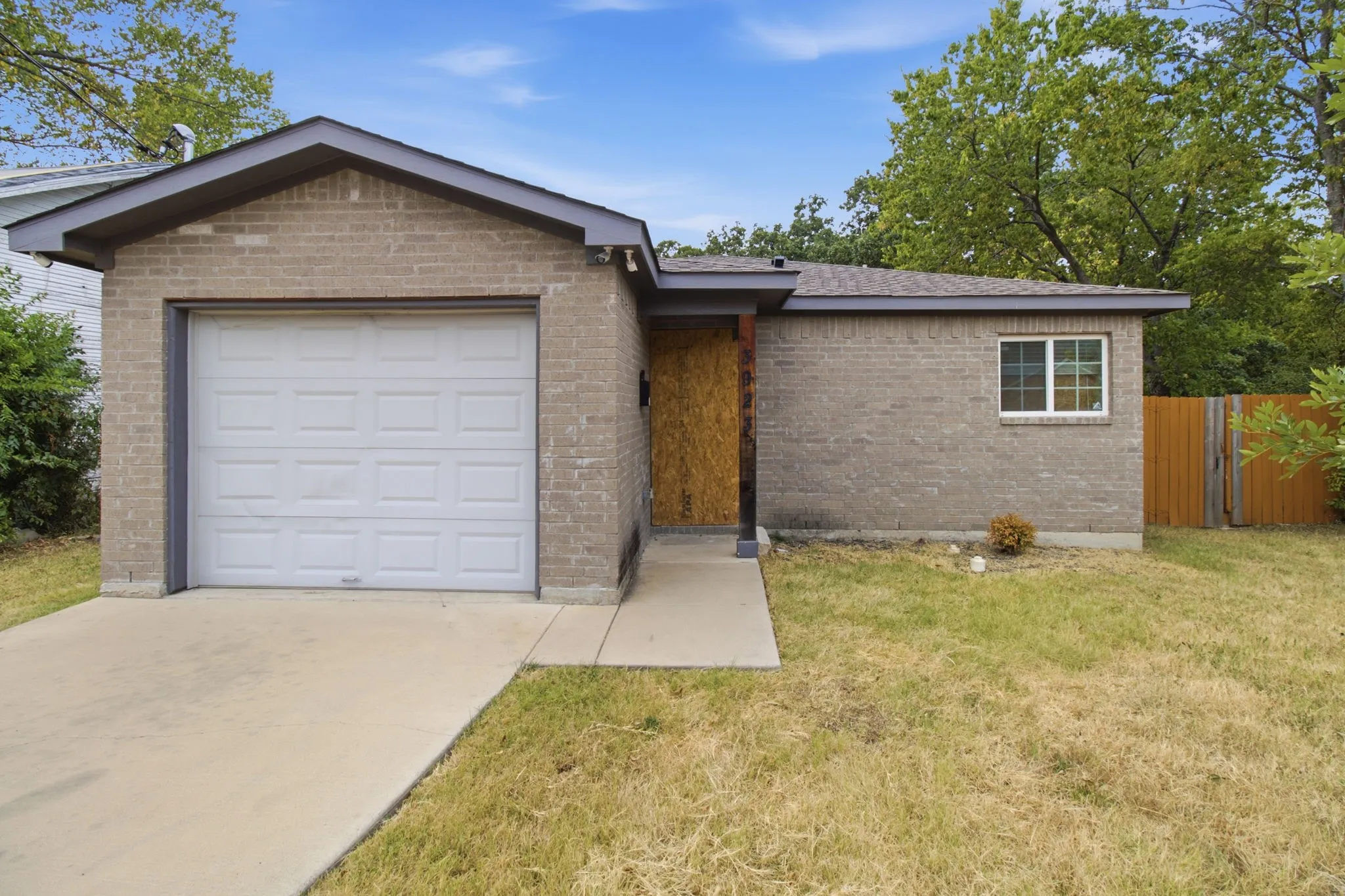 Brick exterior featuring a front-facing garage with a white door, concrete driveway, and a wood fence