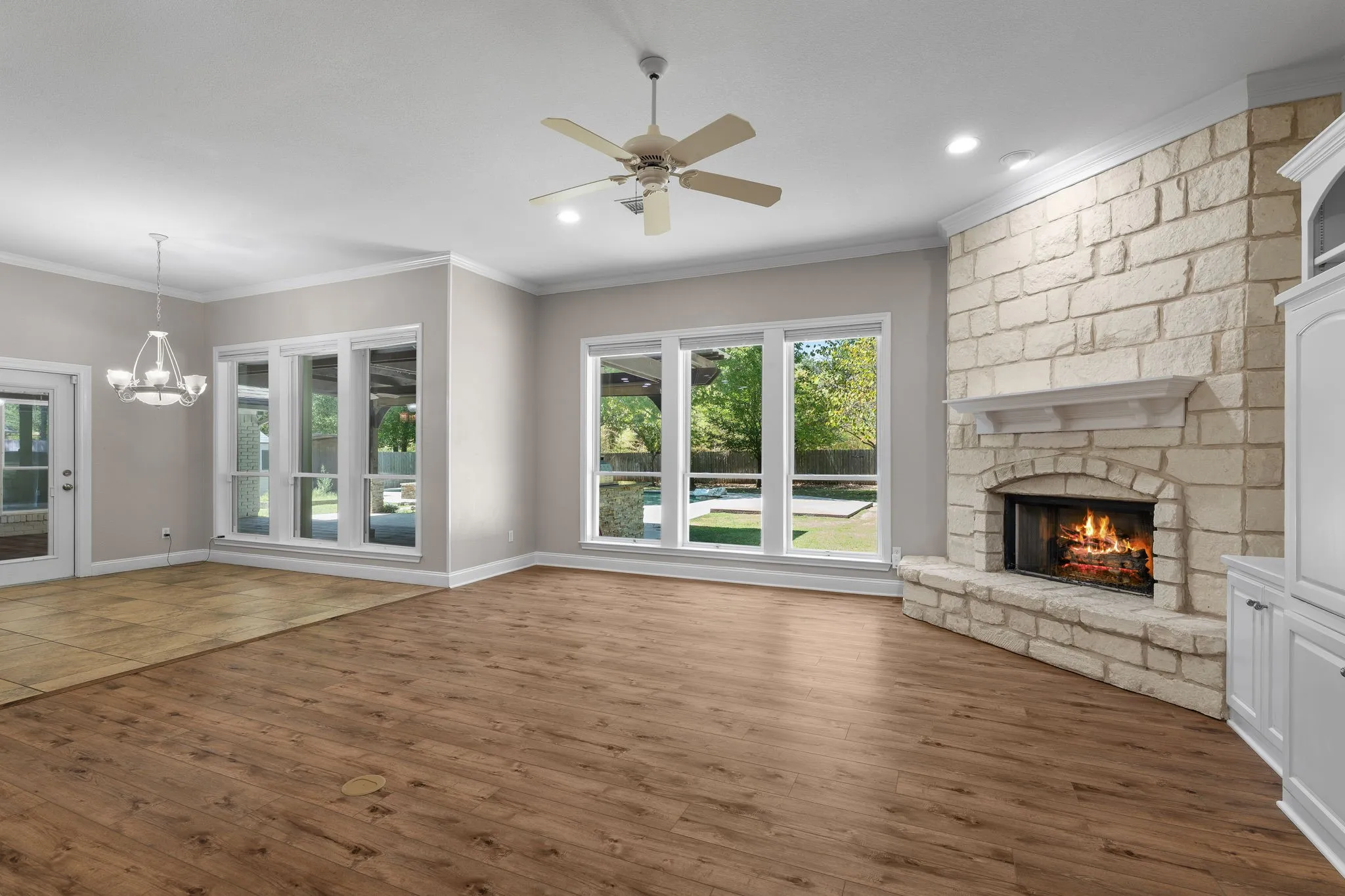 Spacious living area featuring wood-finish flooring, a stone-clad fireplace with a mantel, white built-in cabinetry, and multiple windows