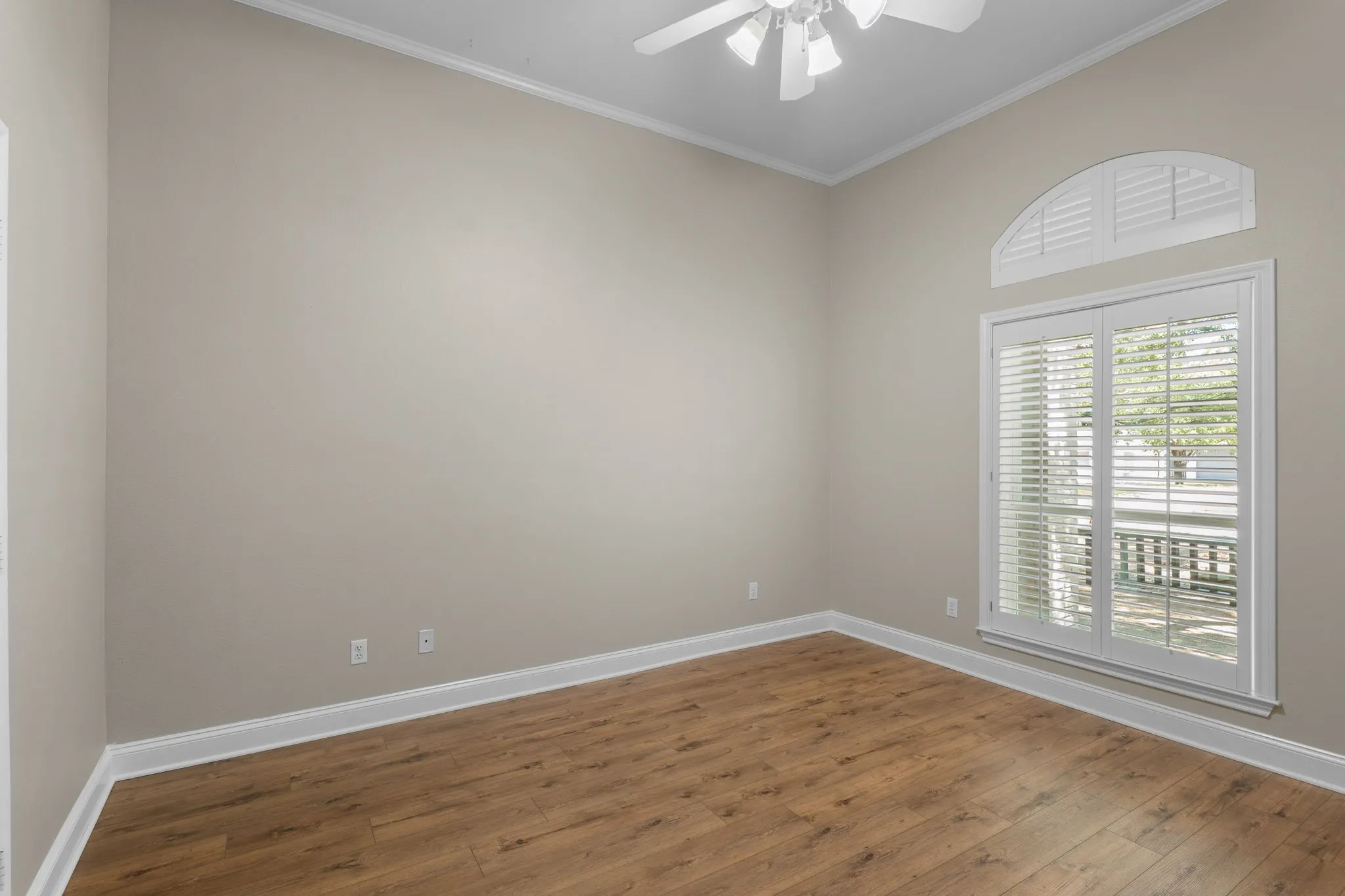 Wood-finish flooring, crown molding, ceiling fan, and arched transom window with plantation shutters