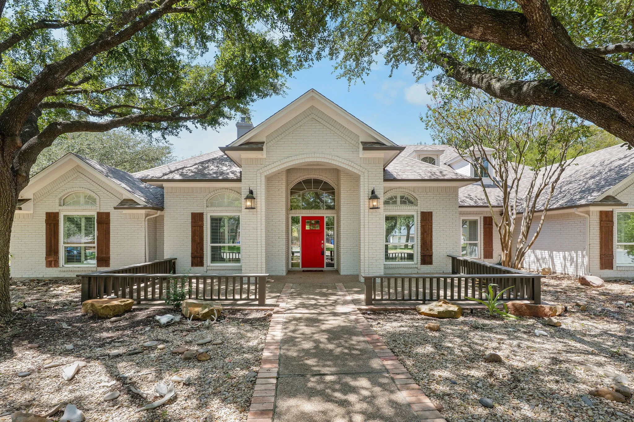 White brick exterior with a prominent red door, arched entry, decorative wood shutters, and exterior lighting fixtures