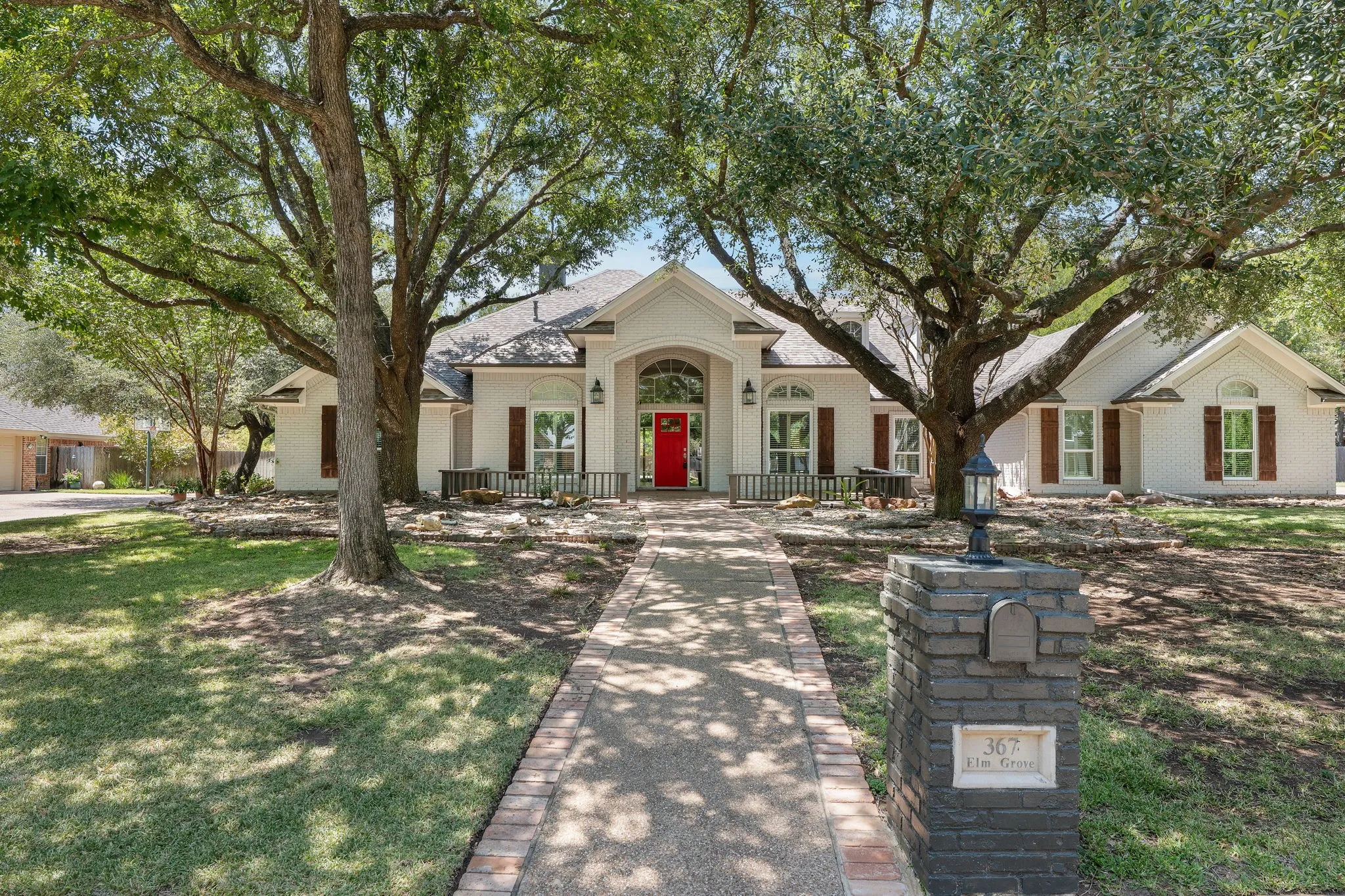 White exterior residence featuring a prominent red entry door, arched transom window, and multiple windows with brown shutters
