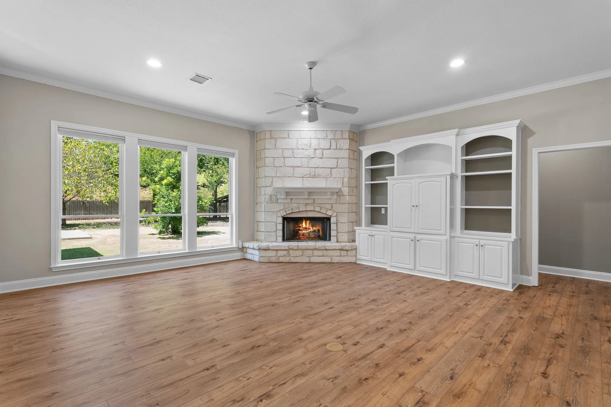 Wood-finish flooring, stone-clad corner fireplace, built-in cabinetry with shelving, recessed lighting, and a ceiling fan