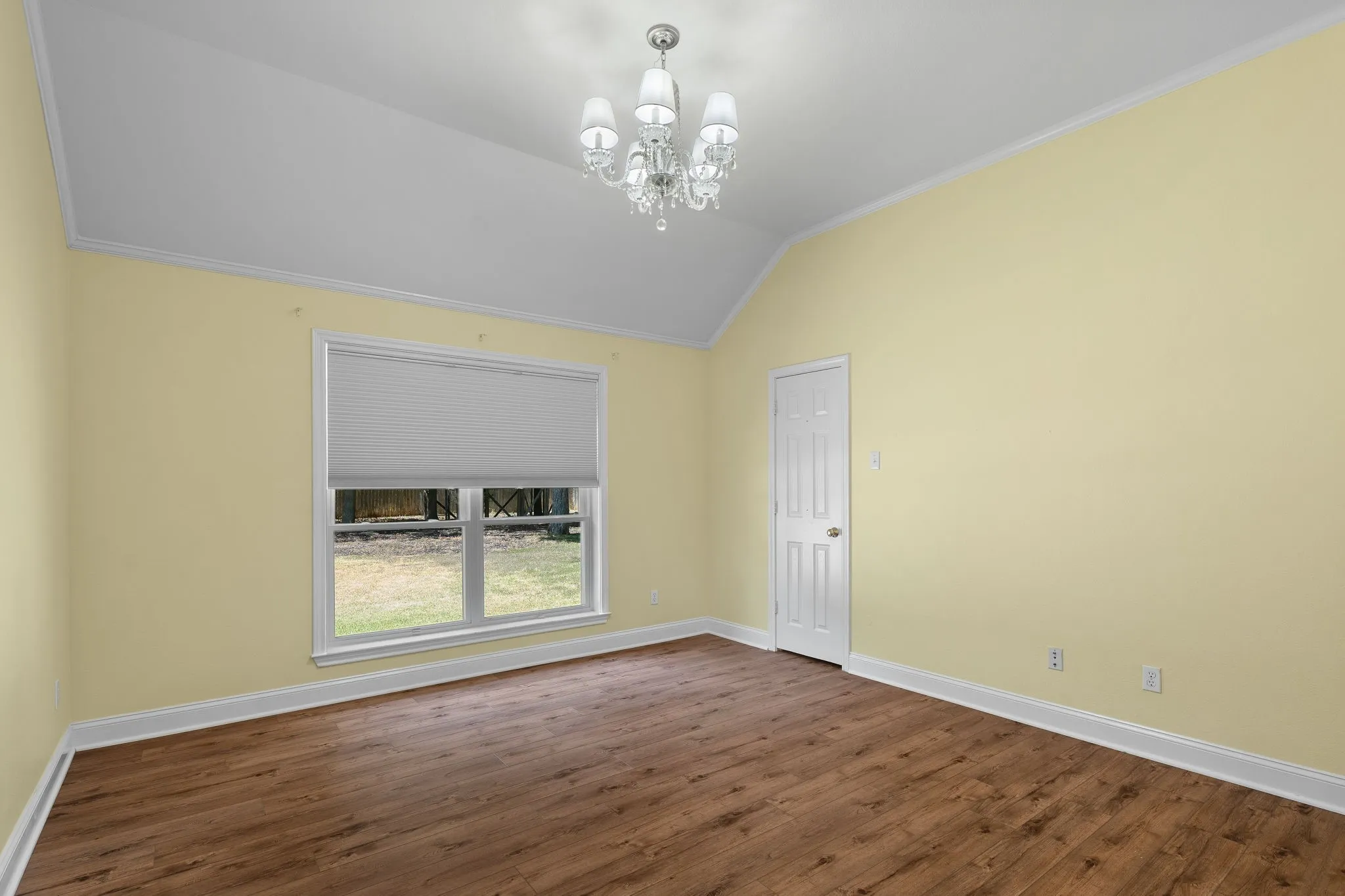 Vaulted ceiling with a crystal chandelier, wood-finish flooring, and a window with a cellular shade