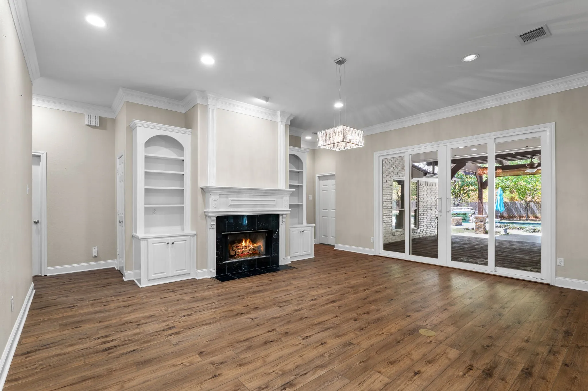 Wood-finish flooring throughout, featuring a fireplace with a dark-tiled surround and white mantelpiece, built-in shelving with lower cabinetry, and large sliding glass doors leading to an outdoor area