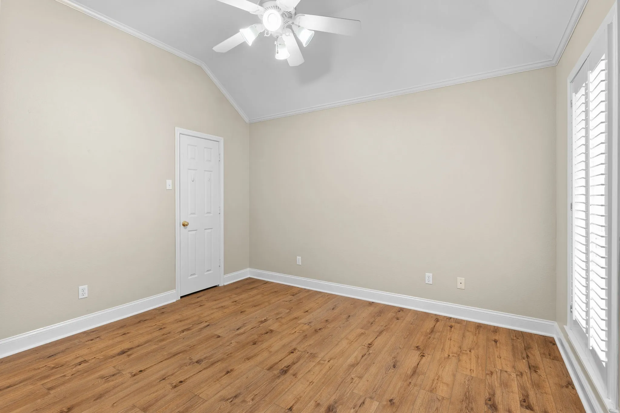 Vaulted ceiling with a white ceiling fan, wood-finish flooring, and crown molding