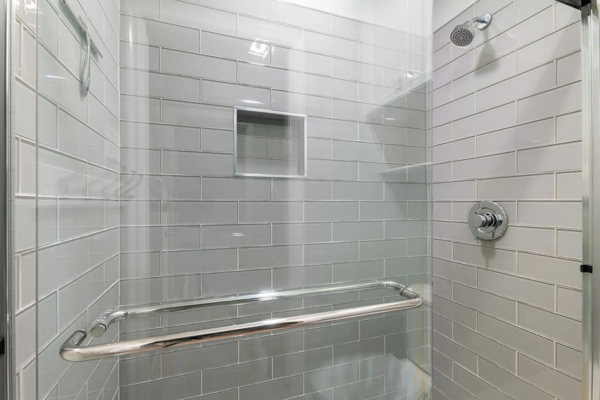 Glass-enclosed shower with subway tile surround, built-in storage niche, and polished chrome fixtures