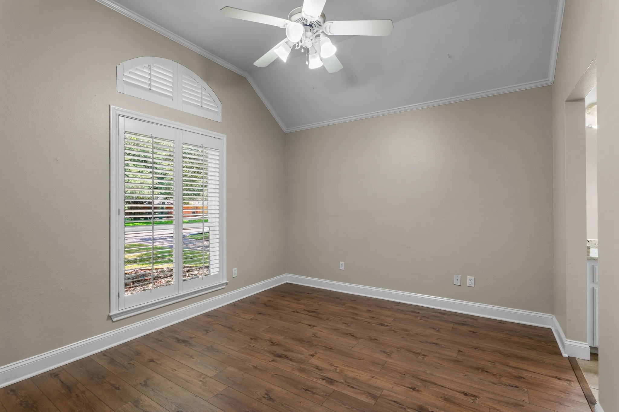 Vaulted ceiling with a ceiling fan, wood-finish flooring, plantation shutters, and crown molding