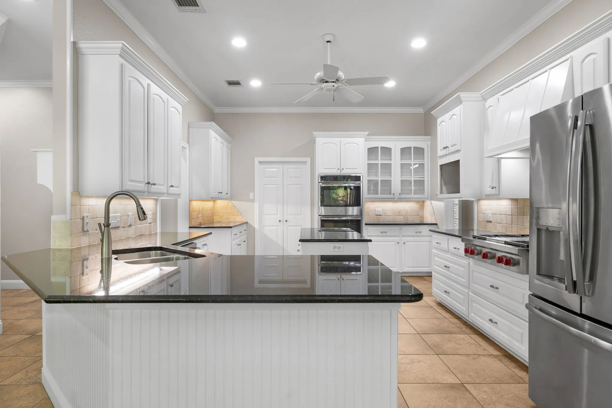 Gourmet kitchen with white cabinetry, stainless steel appliances, stone countertops, integrated sink, and tile flooring