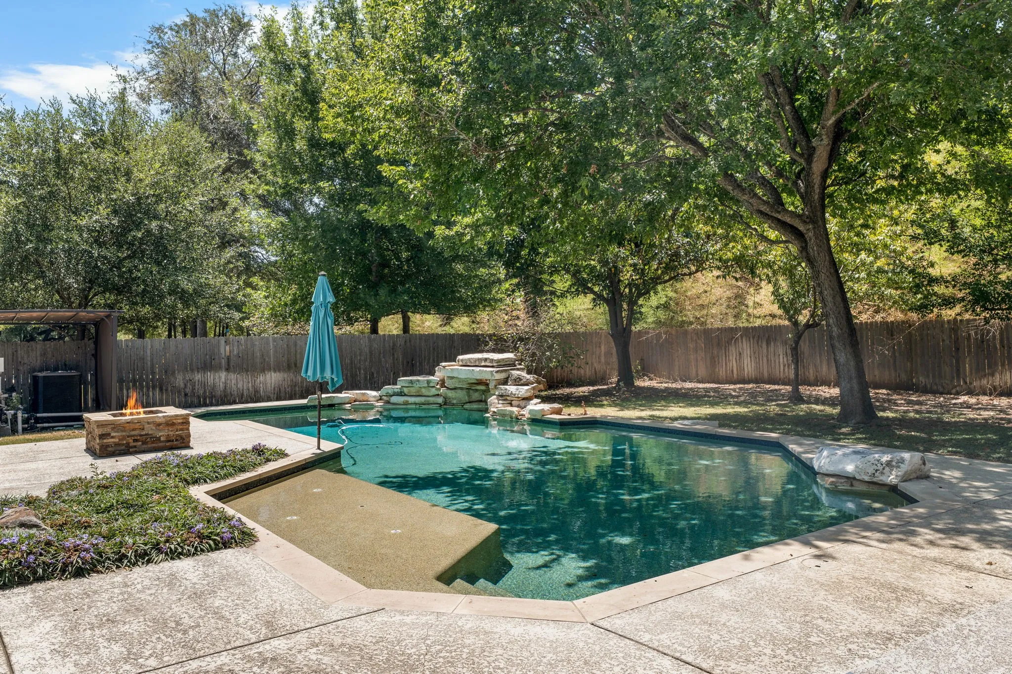In-ground swimming pool featuring a rock waterfall and sun shelf
