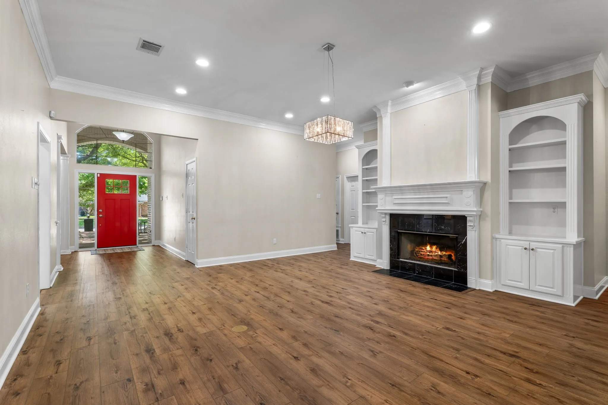 Wood-finish flooring, recessed lighting, crown molding, a decorative fireplace with a dark tile surround, and built-in shelving