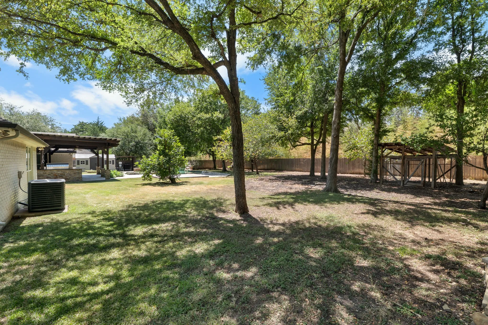 Expansive backyard featuring mature trees, a wooden pergola, and a privacy fence