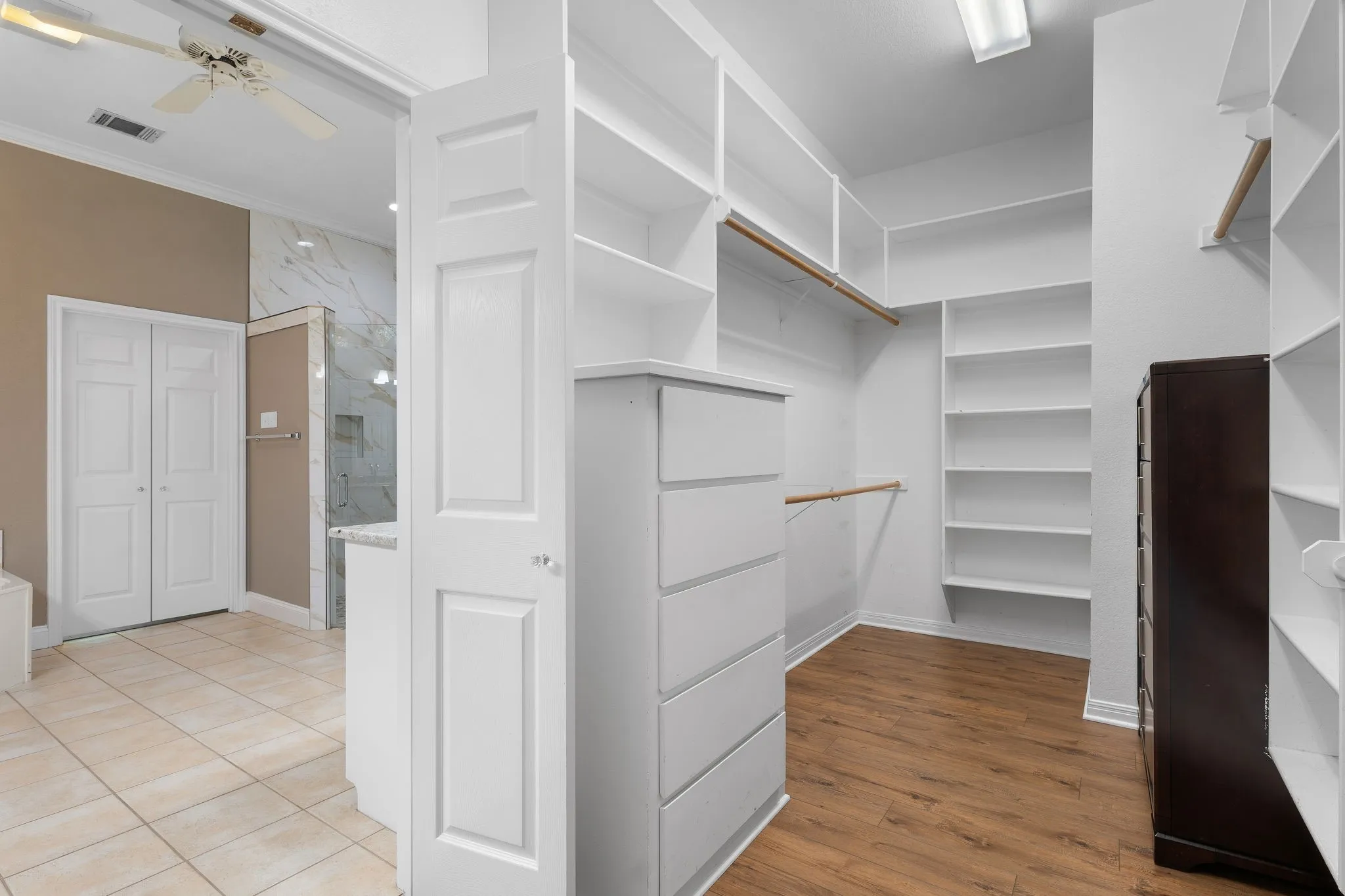 Walk-in closet featuring extensive built-in shelving, wood-finish flooring, and integrated drawer storage