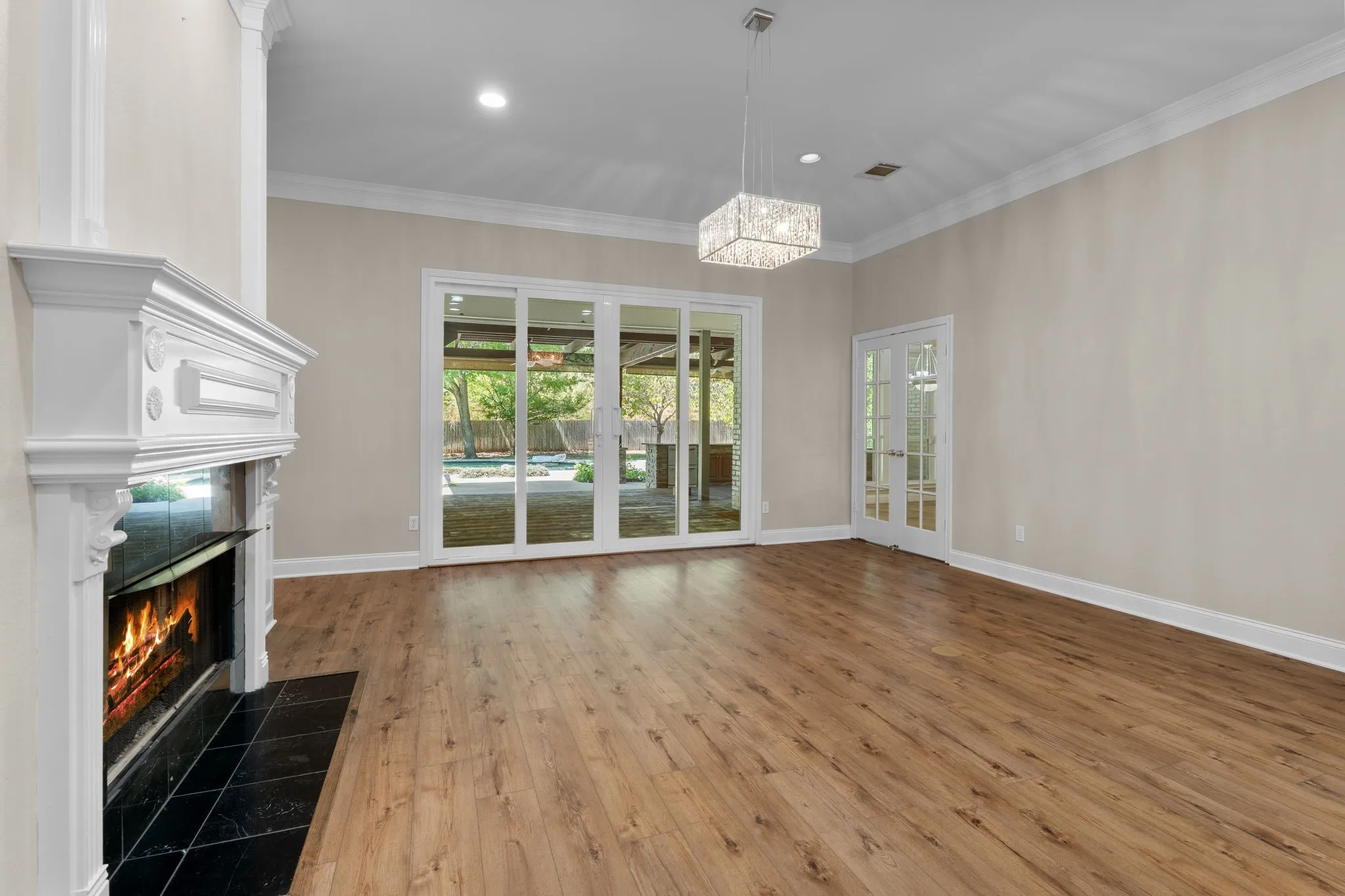 Wood-finish flooring, white fireplace with a black tile hearth, crown molding, double French doors, and sliding glass doors