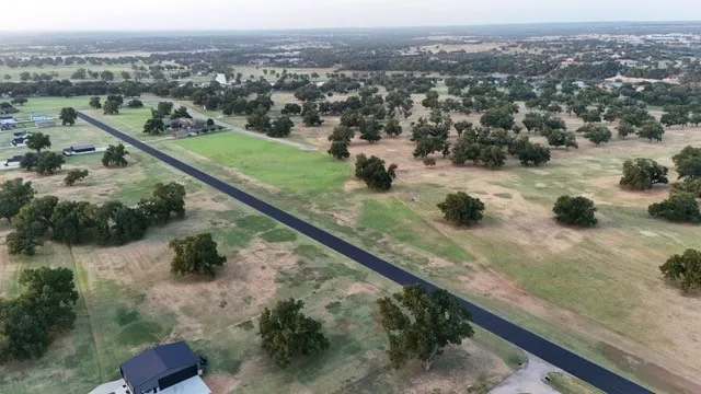 Expansive rural landscape featuring scattered mature trees, a paved roadway, and various residential structures