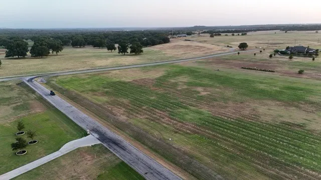 Expansive open fields with mature trees, established roads, and a visible residential structure in the distance
